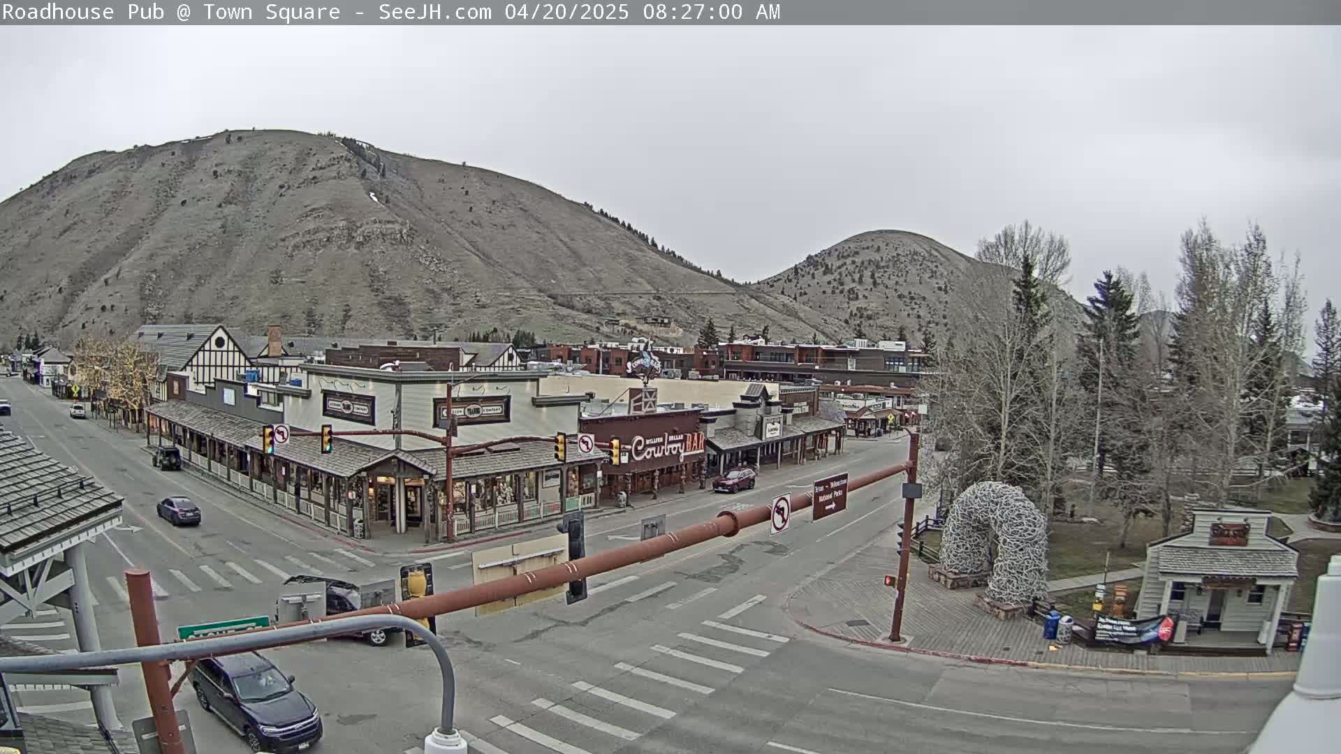A town square nestled between two mountains under an overcast sky, with several shops and cars visible on the street.