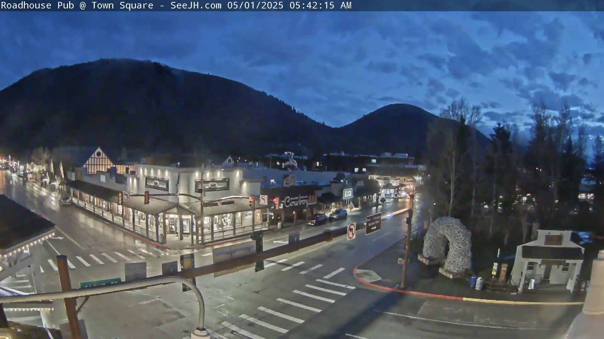 A wet town square at twilight, nestled between dark mountains under a cloudy sky.