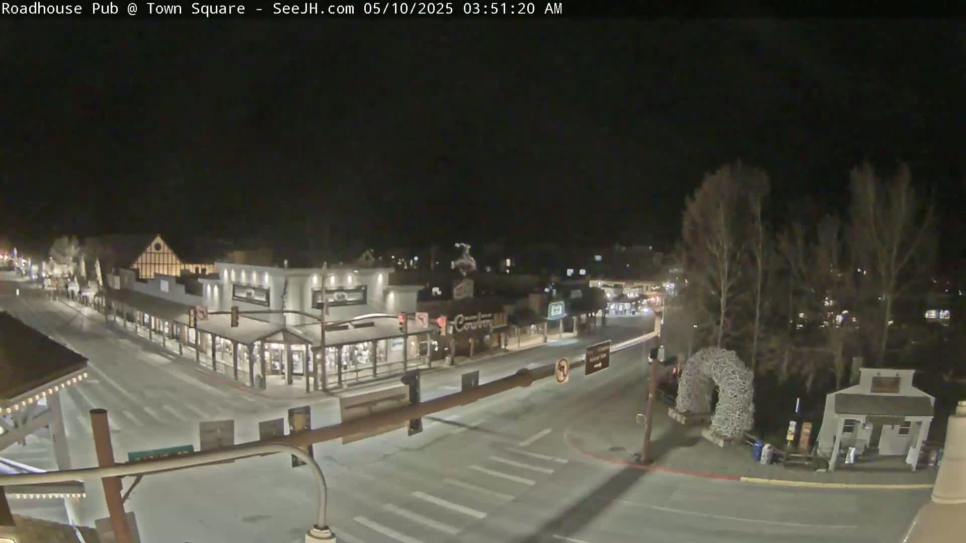 A nighttime, overhead view of a snow-covered town square with several buildings and relatively empty streets.