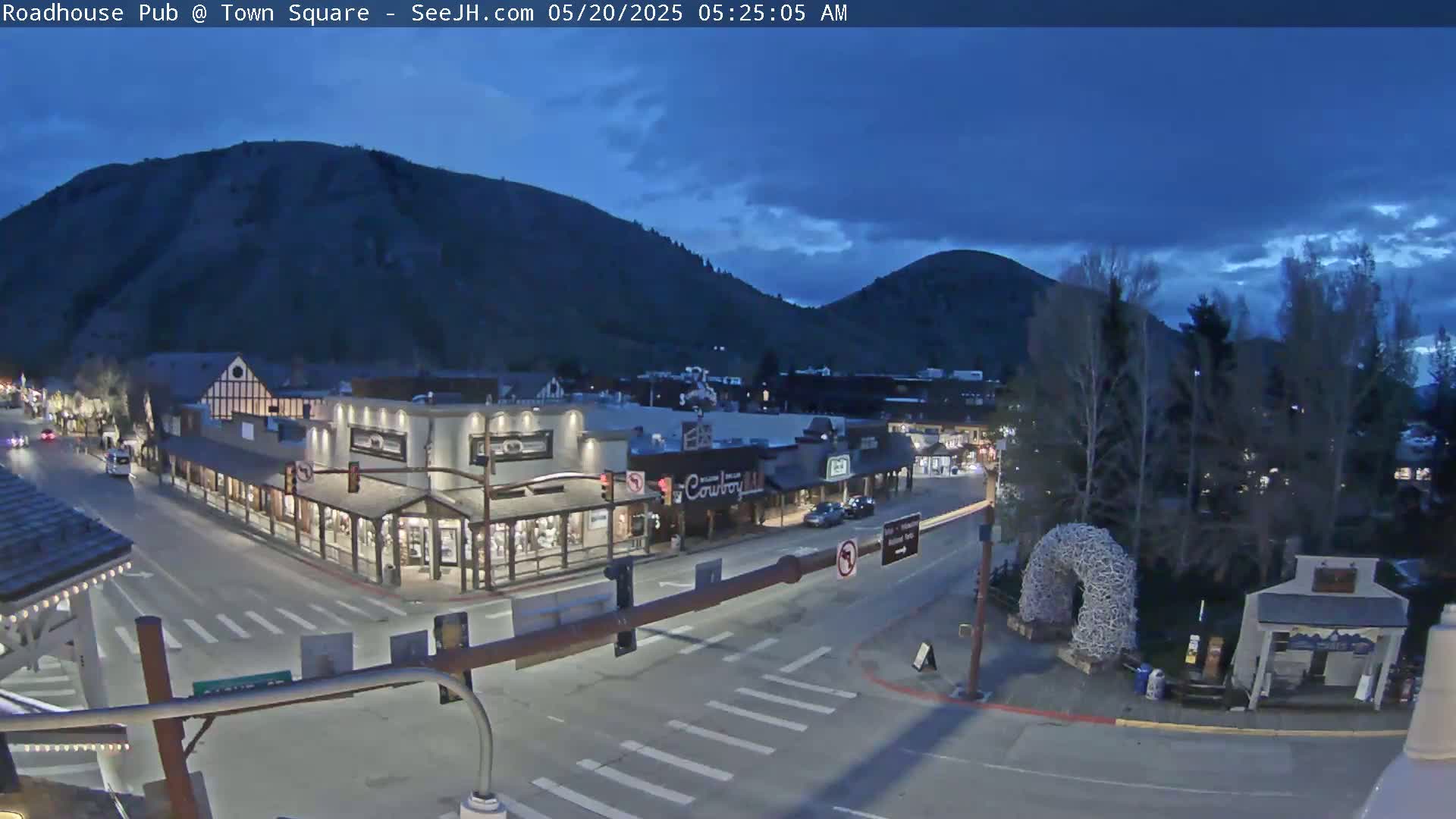 A nighttime view of a town square nestled between mountains, under a mostly clear, dark blue sky.