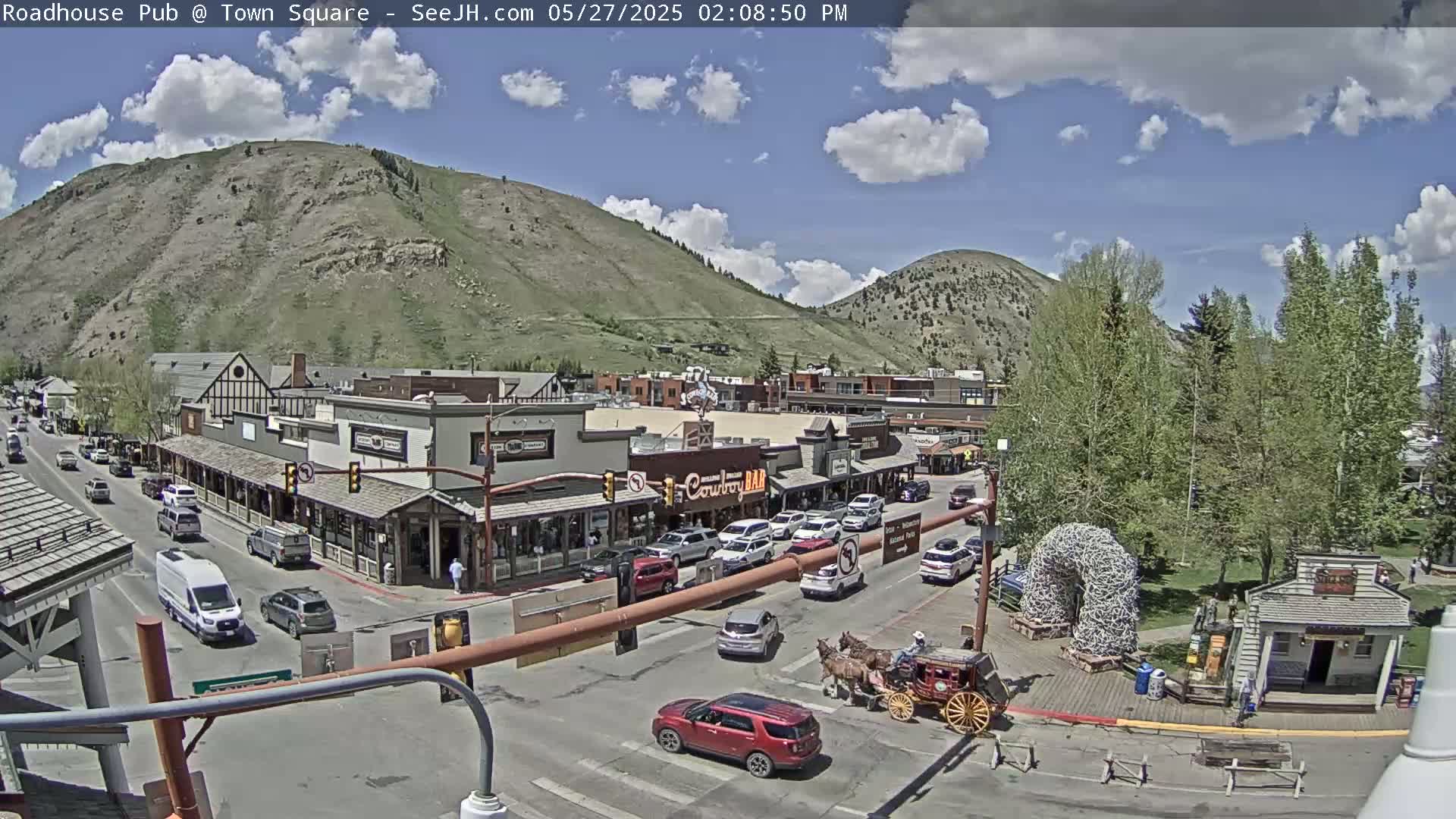 A partly sunny day shows a town square with buildings, cars, a horse-drawn carriage, and a large hill in the background.