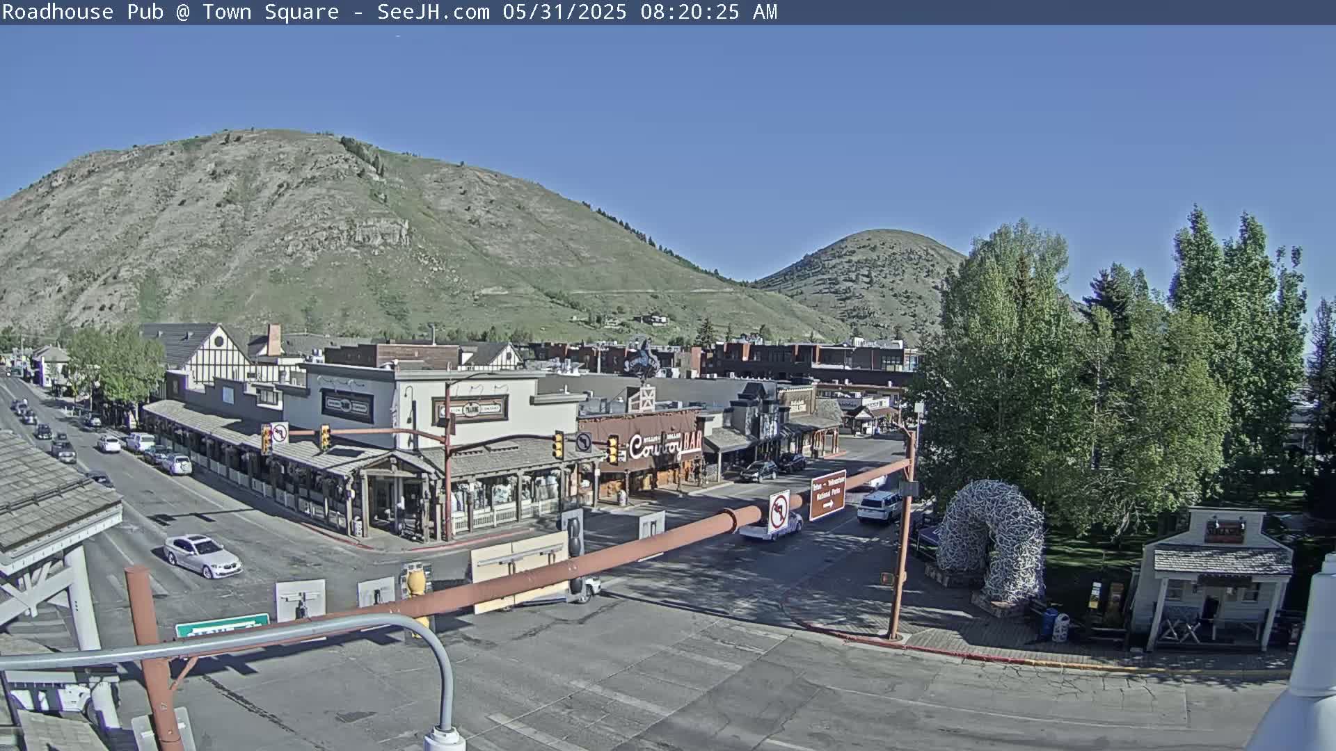 A town square with buildings, cars, and a large horseshoe-shaped sculpture sits under a clear blue sky, nestled between two hills.