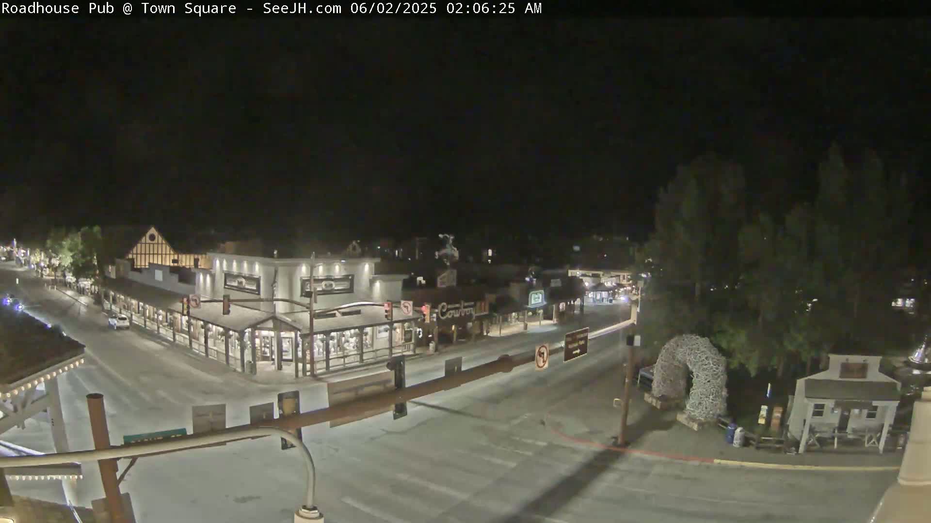 A nighttime, high-angle view shows a quiet town square with several buildings and a few vehicles on the road.