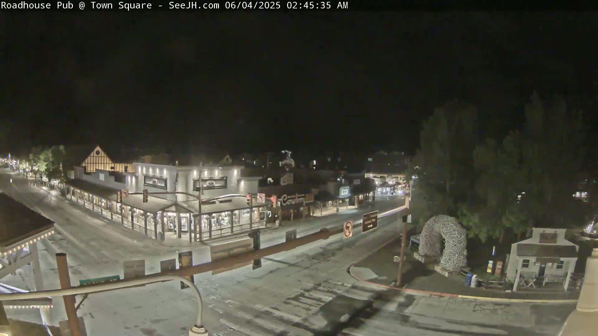 A snow-dusted town square at night, showing several buildings and a street intersection with minimal traffic.