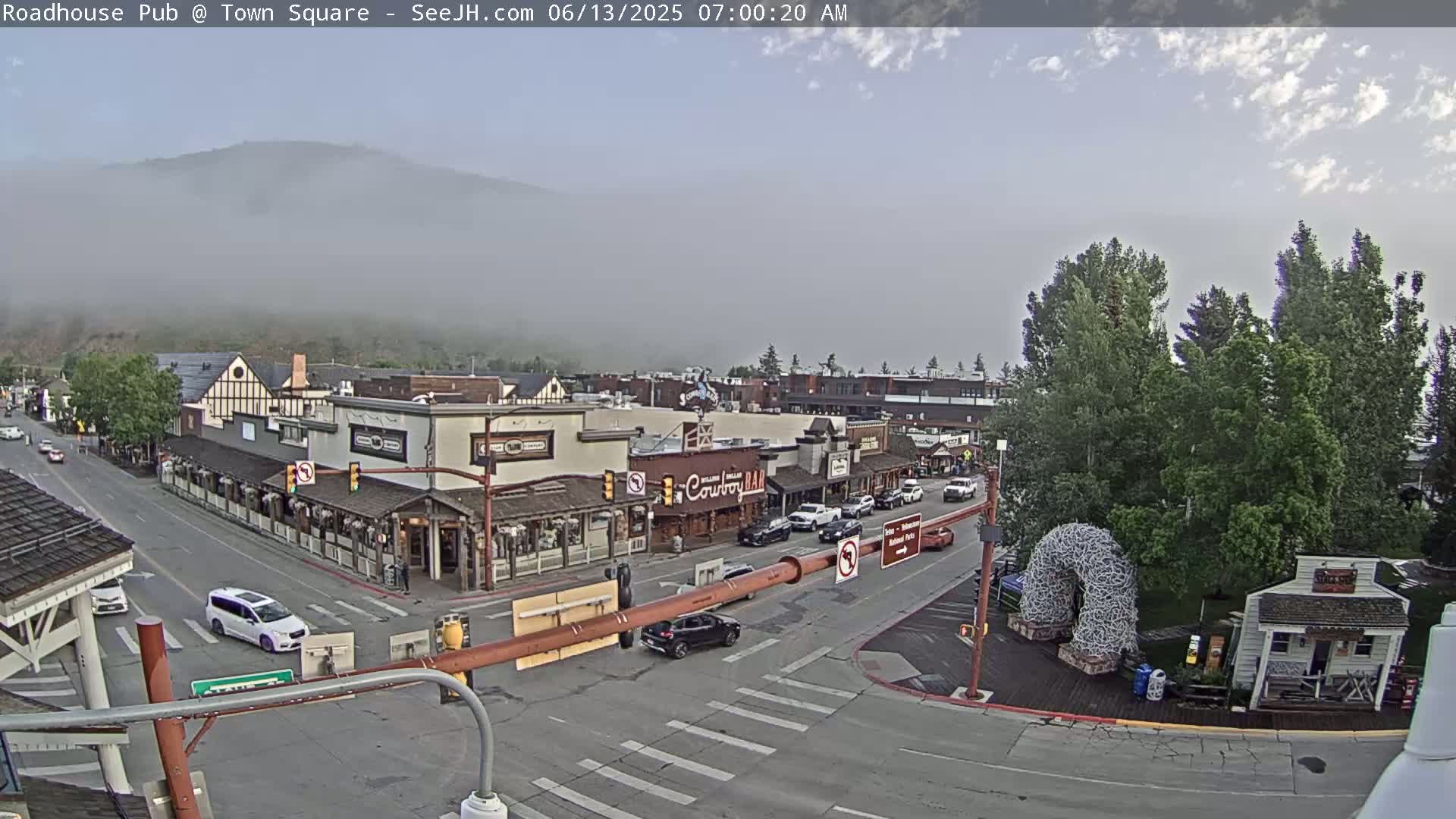 A foggy mountain overlooks a town square with several buildings, including a saloon, and cars driving on intersecting streets.