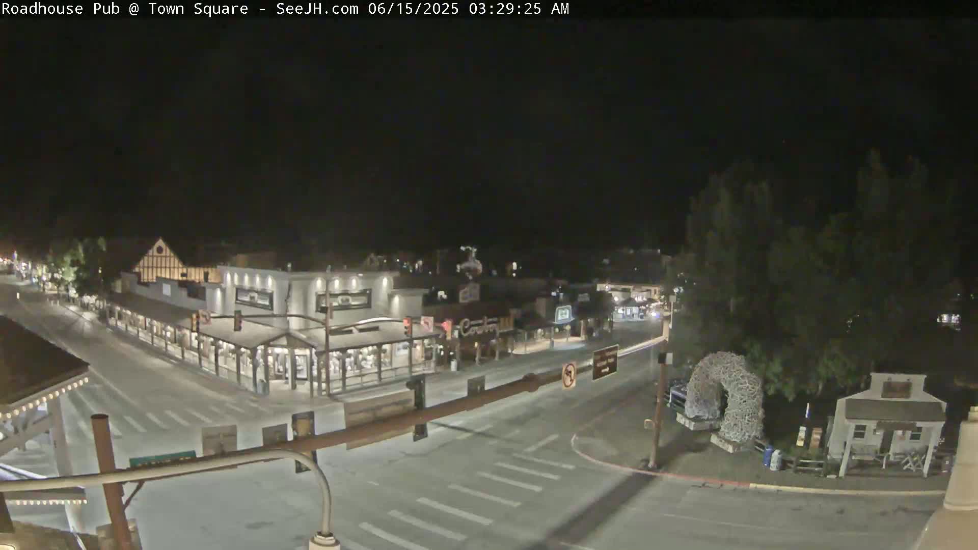 A nighttime, high-angle view shows a mostly empty town square with several buildings, including a pub, and a few cars at intersections.