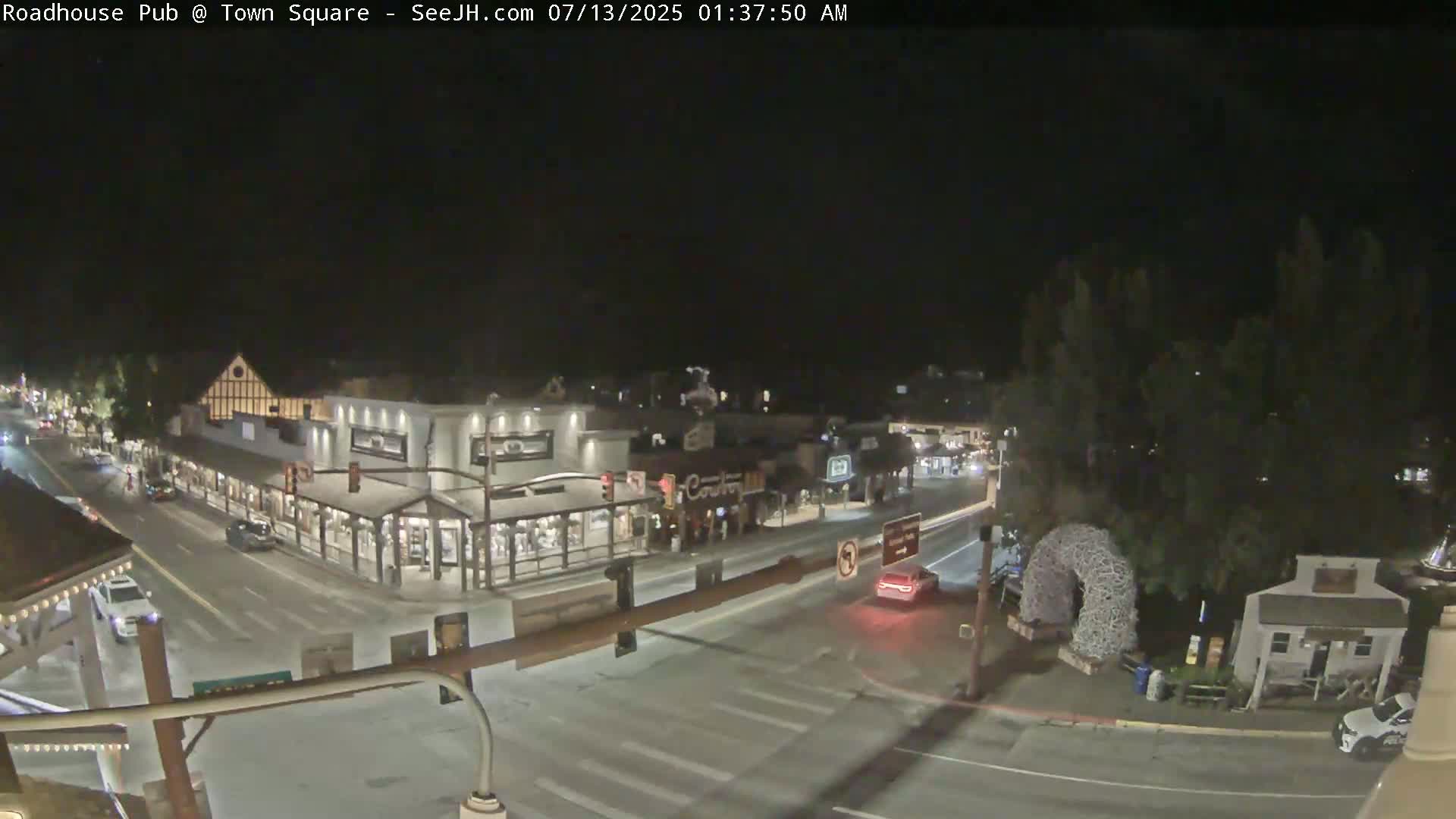 A nighttime view of a town square with several buildings and vehicles, under clear skies.