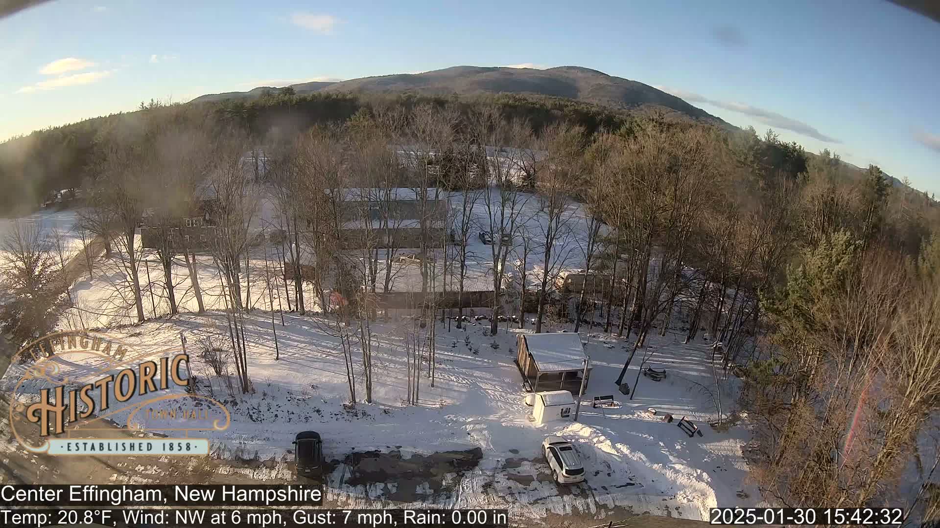 A snow-covered landscape with buildings and trees, viewed from above under a mostly clear sky.