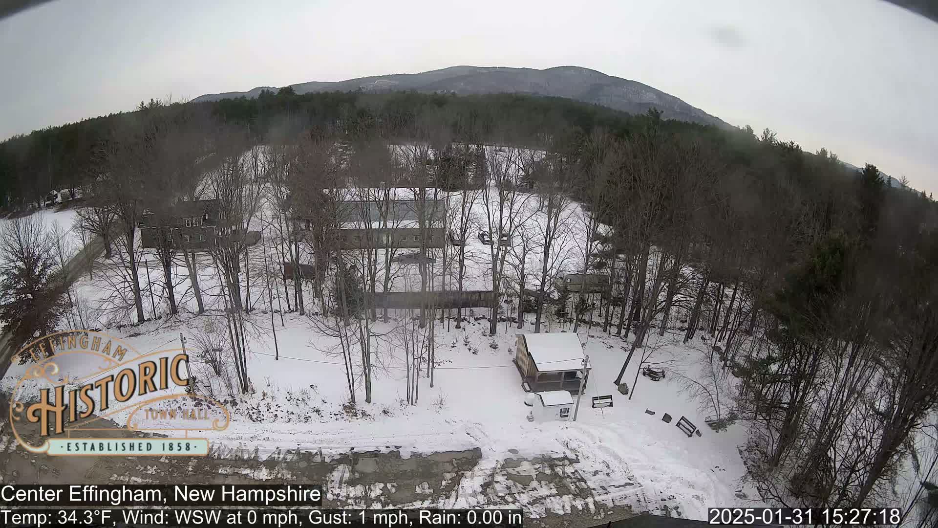 A snow-covered landscape with bare trees, several buildings, and a small shed is visible beneath a cloudy sky.