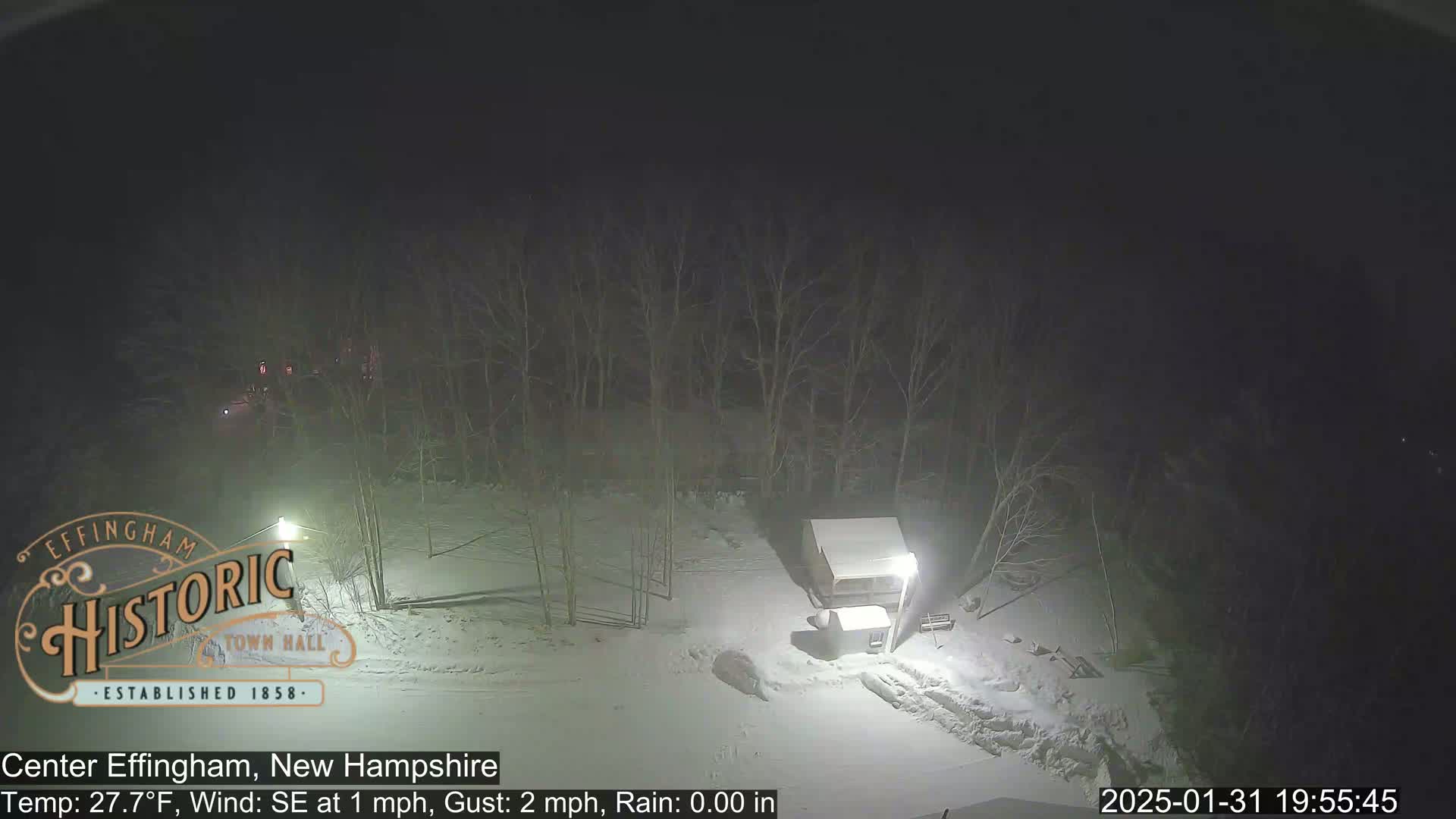 A nighttime snow-covered scene shows a small structure and bare trees under a dark sky.