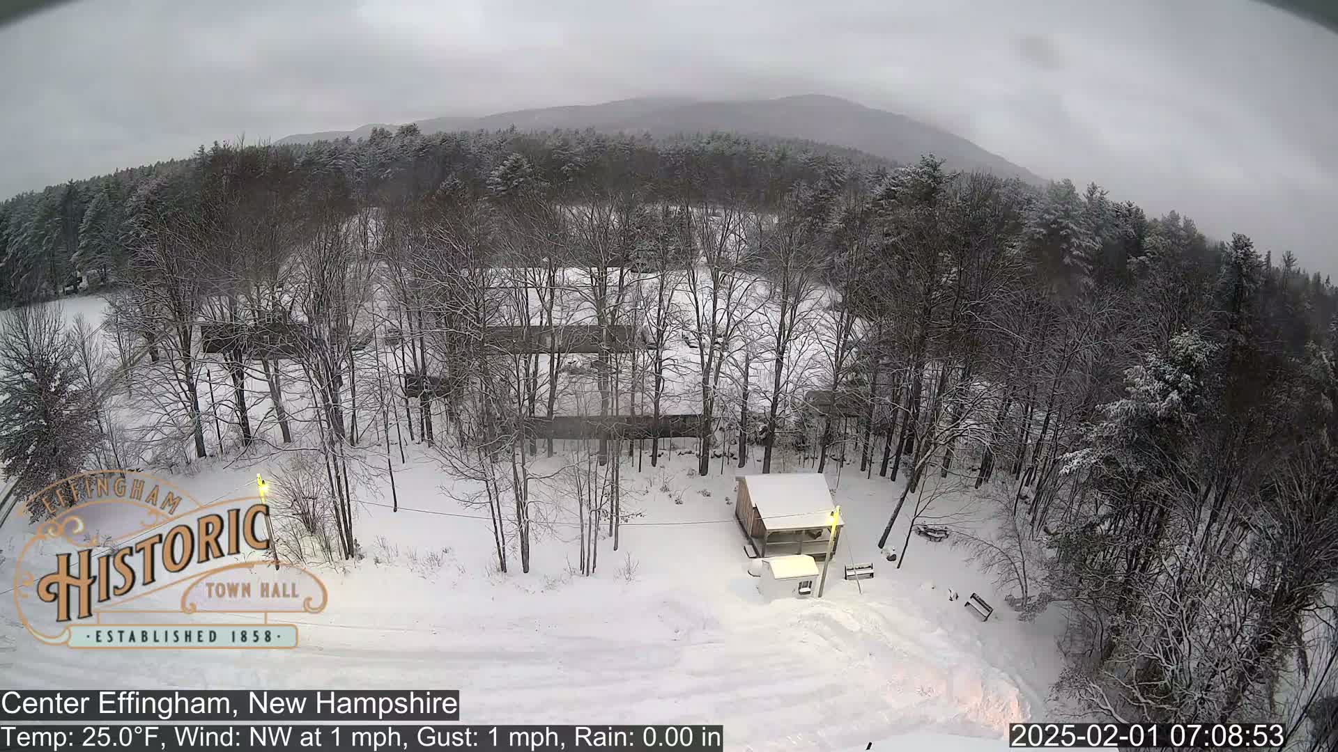 A snow-covered landscape with leafless trees and a small building, under an overcast sky.
