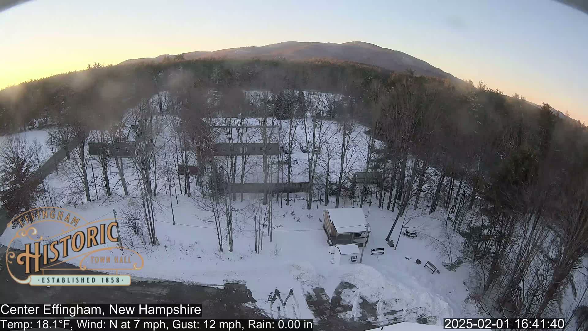 A snow-covered landscape with bare trees and a few buildings is visible beneath a clear, twilight sky, with mountains in the distance.