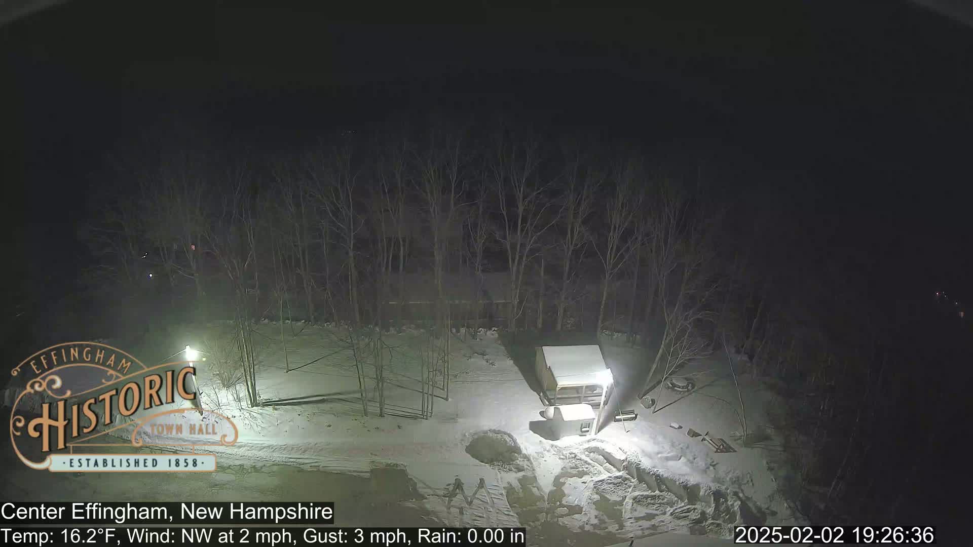 A nighttime, snow-covered scene shows bare trees, a small shed, and some equipment under a dark sky with a northwest wind.