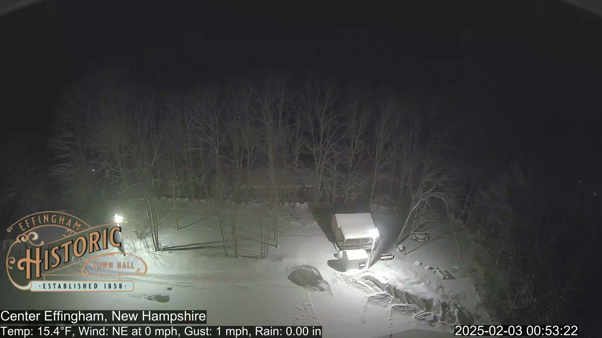 A nighttime, snow-covered scene shows a small building and bare trees under a dark sky with a light northeast wind and no rain.