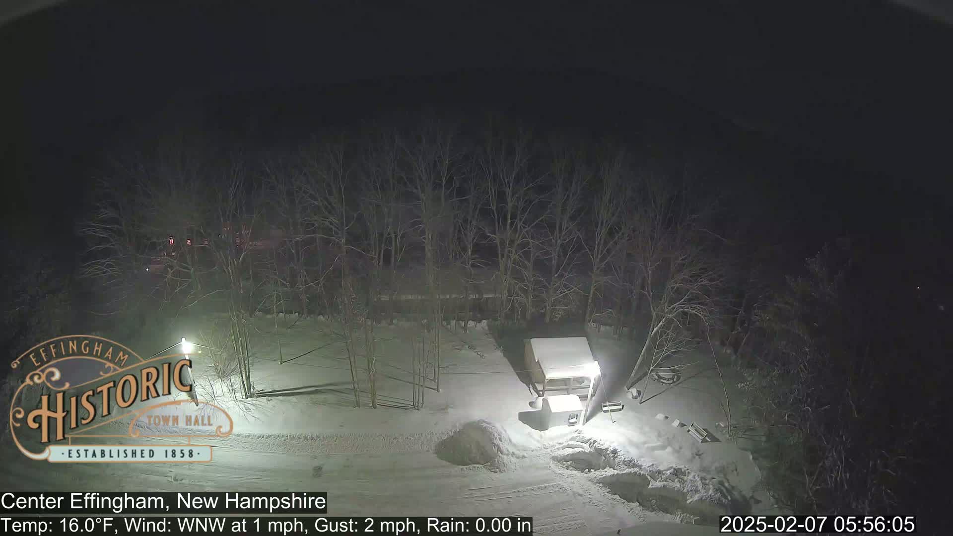 A snow-covered nighttime scene shows a small structure and bare trees under a dark sky.