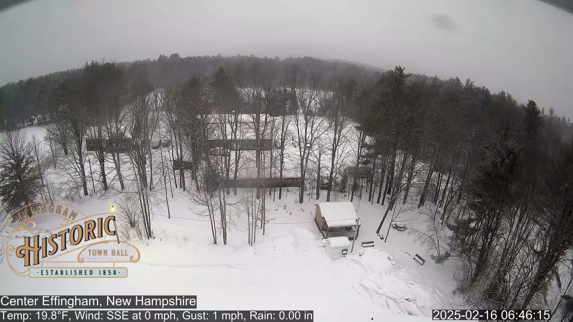 A snow-covered landscape with leafless trees and a small structure, under an overcast sky.