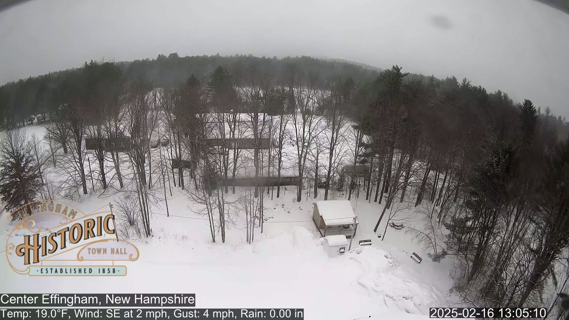 A snow-covered landscape with leafless trees and a small building is visible under an overcast sky.
