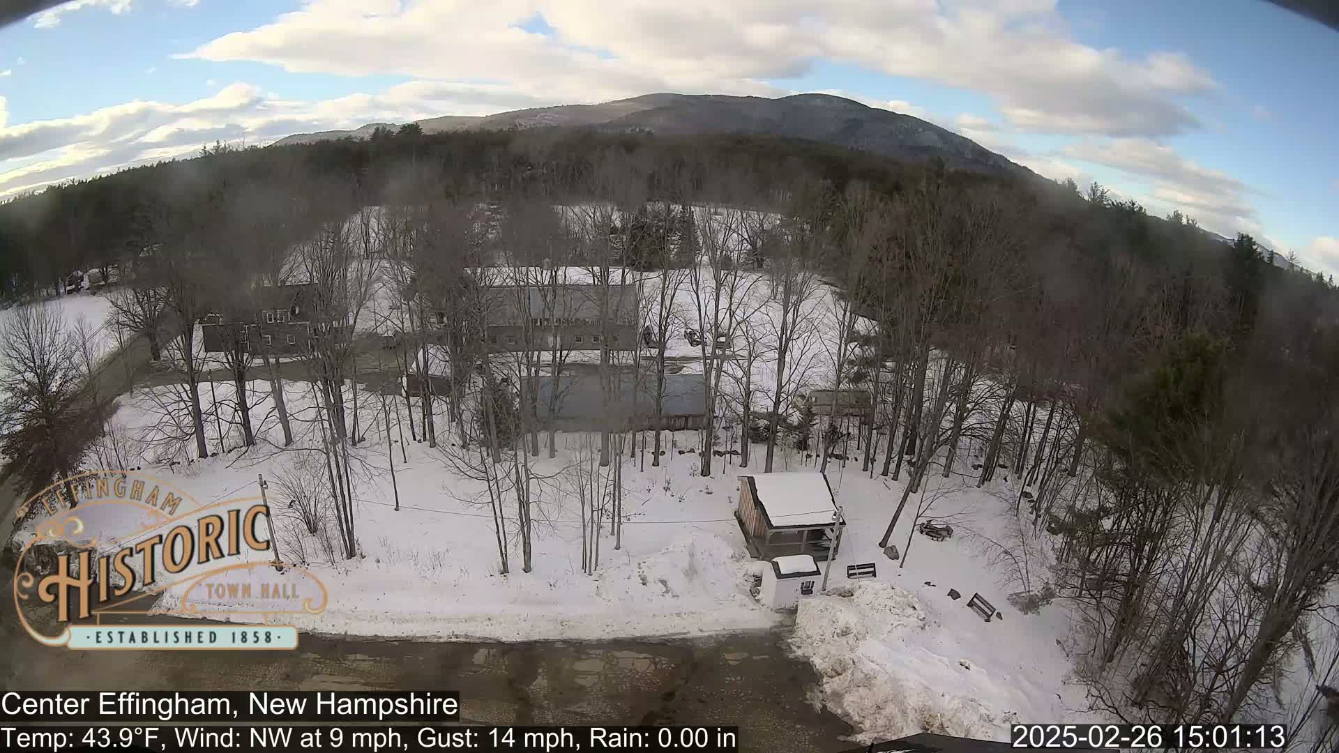 A snow-covered landscape with bare trees and several buildings is visible under a partly cloudy sky.