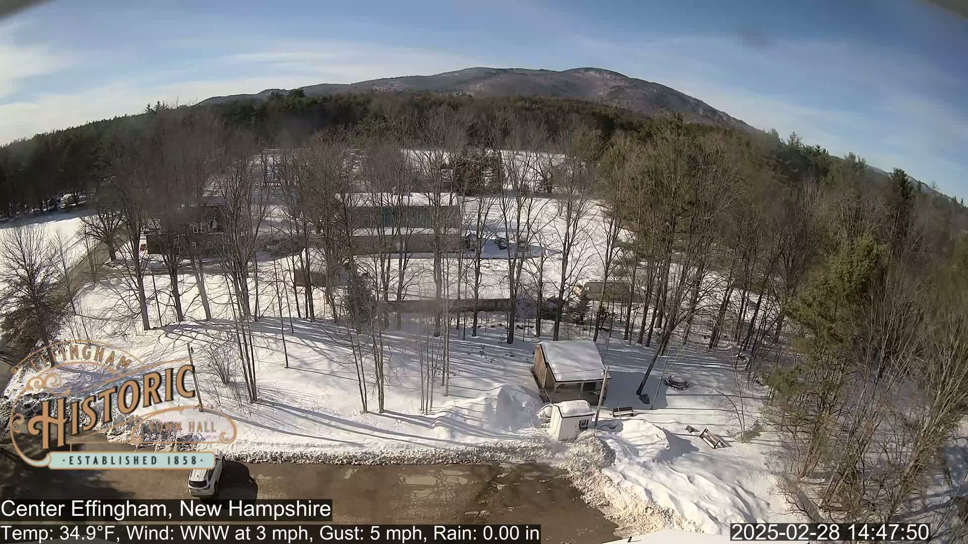 A snow-covered landscape with bare trees and a few buildings is visible under a mostly sunny sky.
