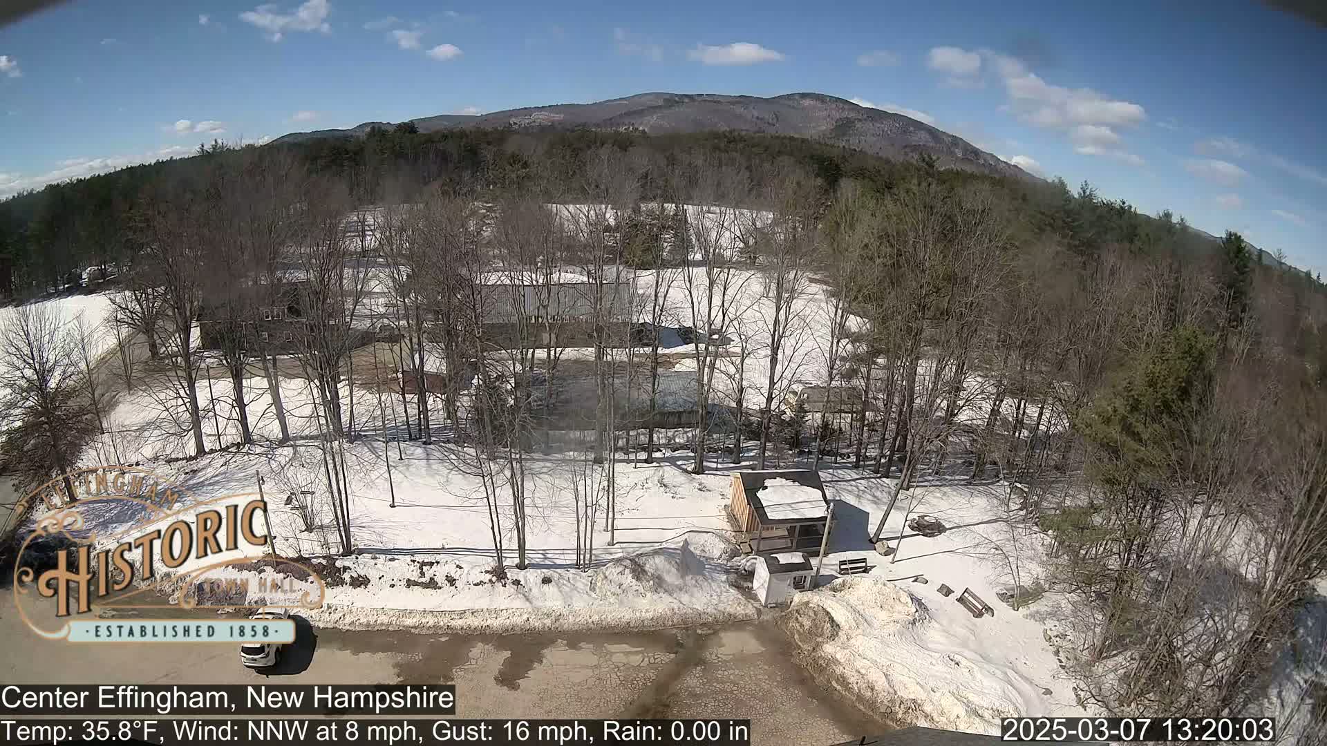 A snow-covered landscape with bare trees and several buildings is visible under a partly sunny sky.