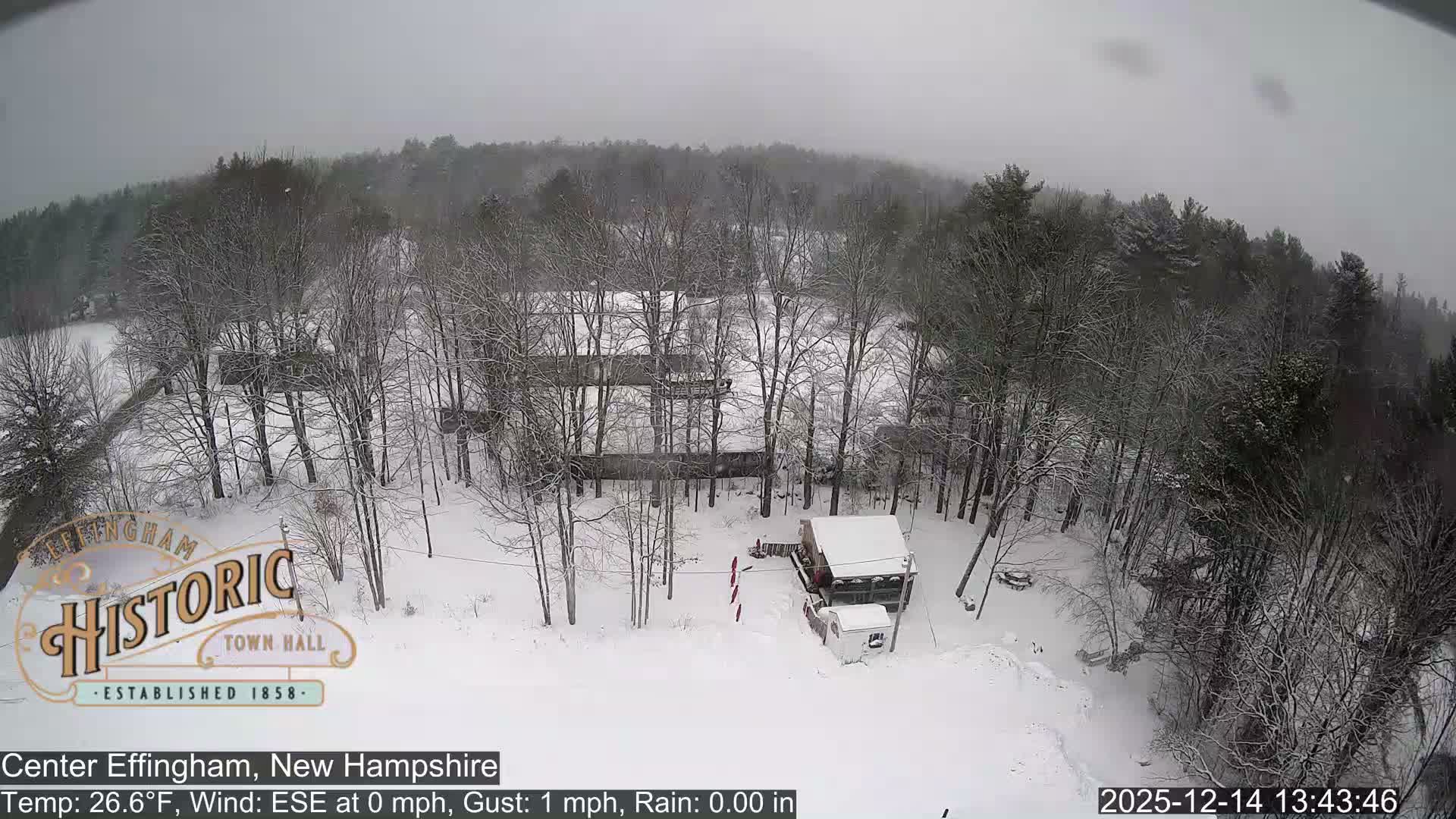 A snowy outdoor scene at night features a brightly lit snowplow actively clearing snow from a path or lot, under clear and cold conditions.