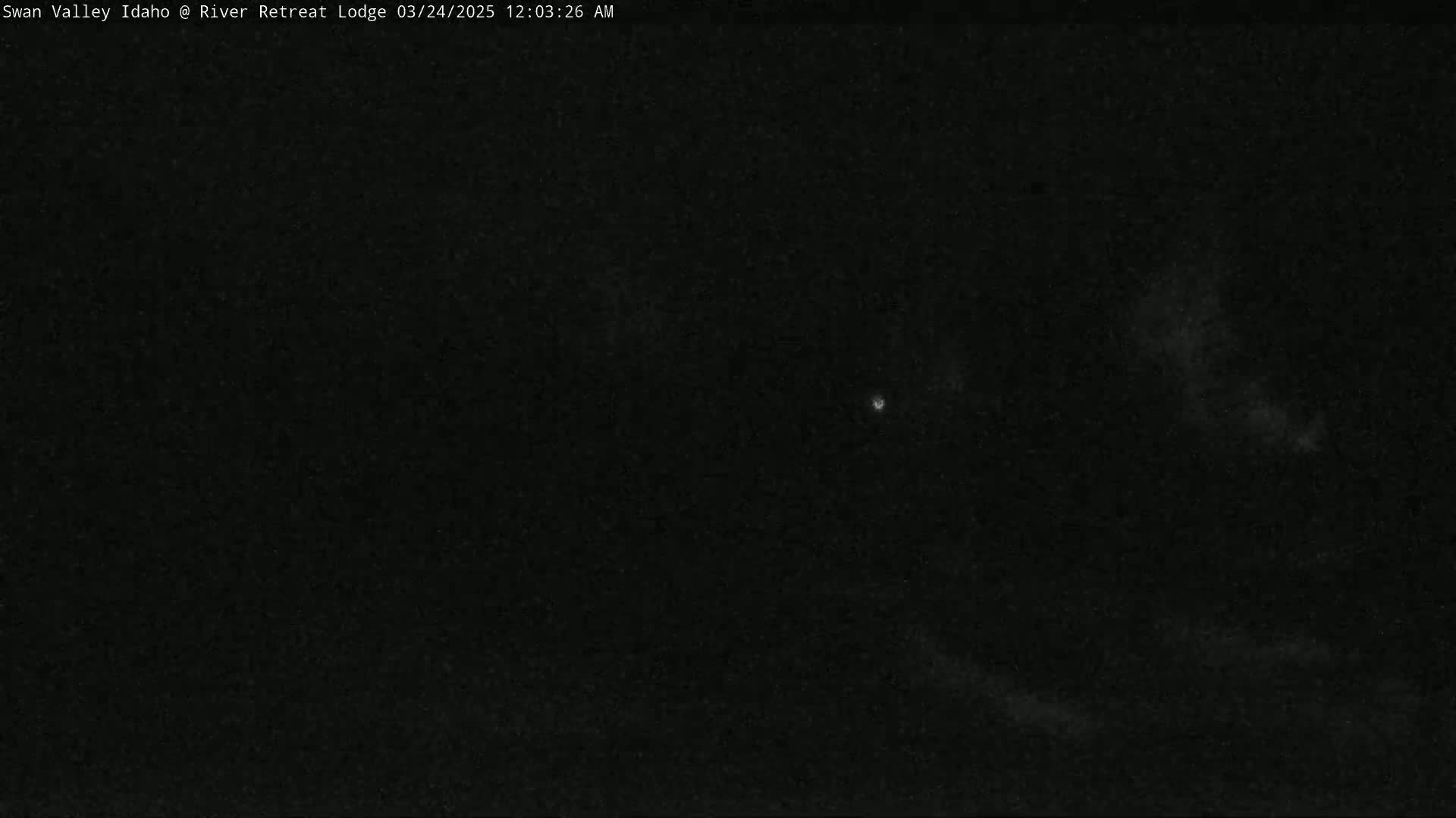 A dark nighttime scene shows a mostly clear sky with a few faint clouds and a single bright light.