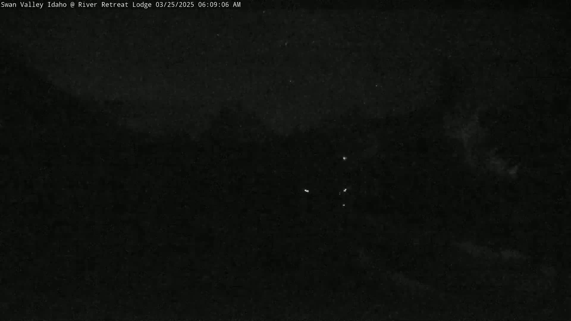 A nighttime, dark outdoor scene shows a few faint lights in the distance under a mostly clear sky.