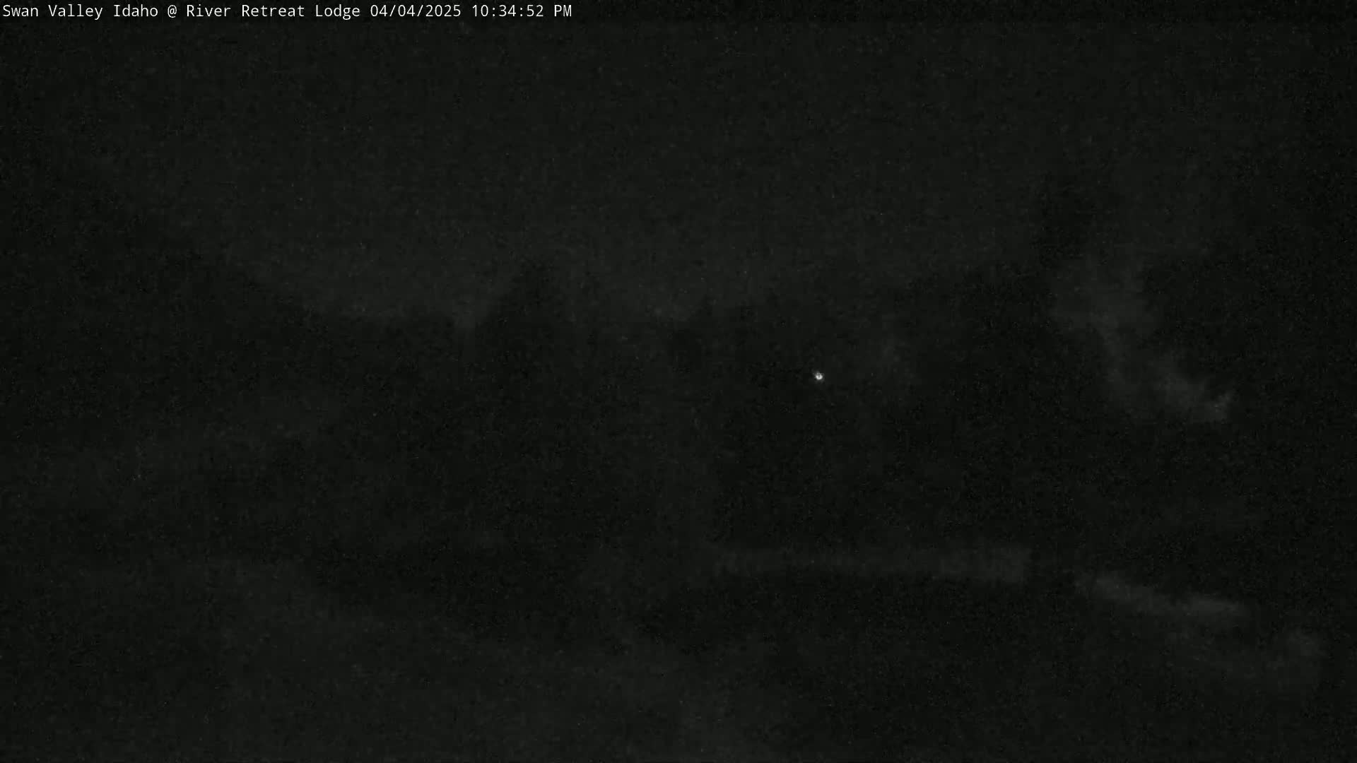 A nighttime, low-light image shows a dark landscape with a few faintly visible lights in the distance.