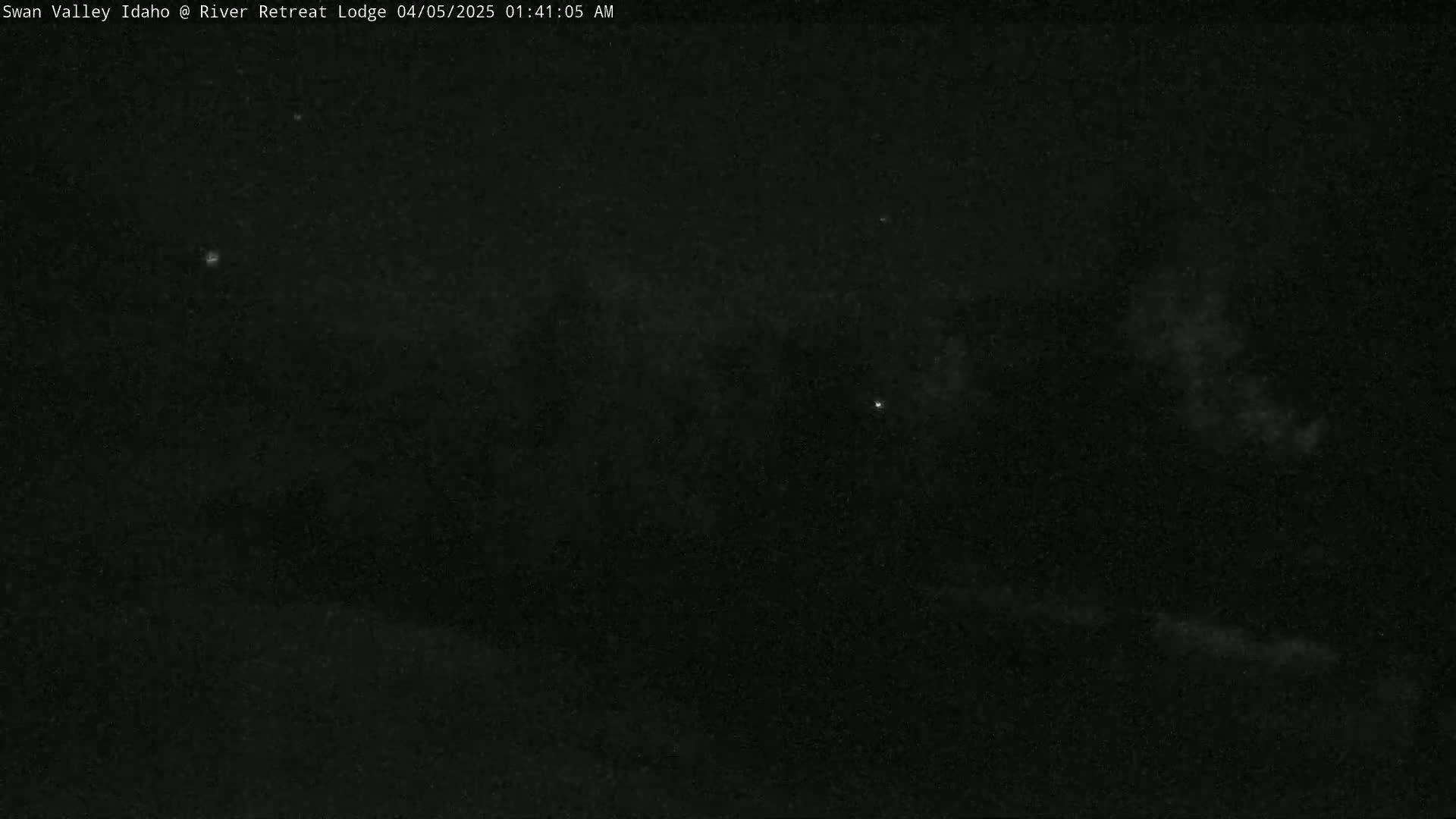 A dark, nighttime scene shows a mostly clear sky with a few faint clouds and some distant, bright lights.