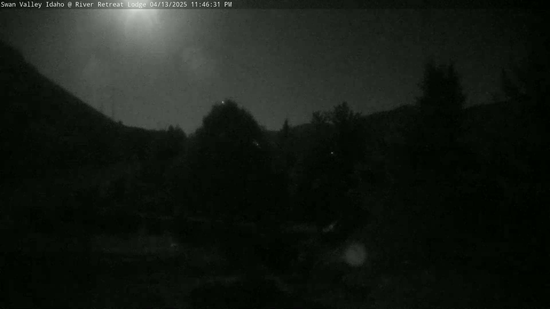 A nighttime, low-light image shows a dark, hilly landscape with some trees and a somewhat cloudy sky.
