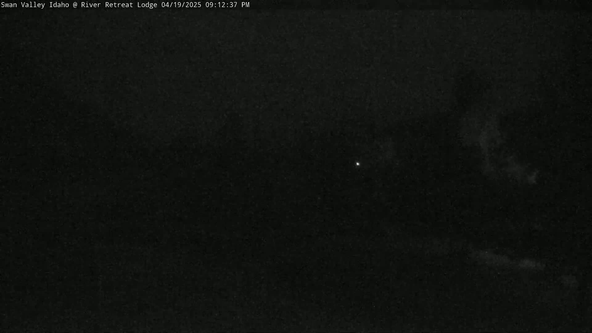 A dark, nighttime outdoor scene shows a mostly clear sky with a few faint clouds and a single bright light.