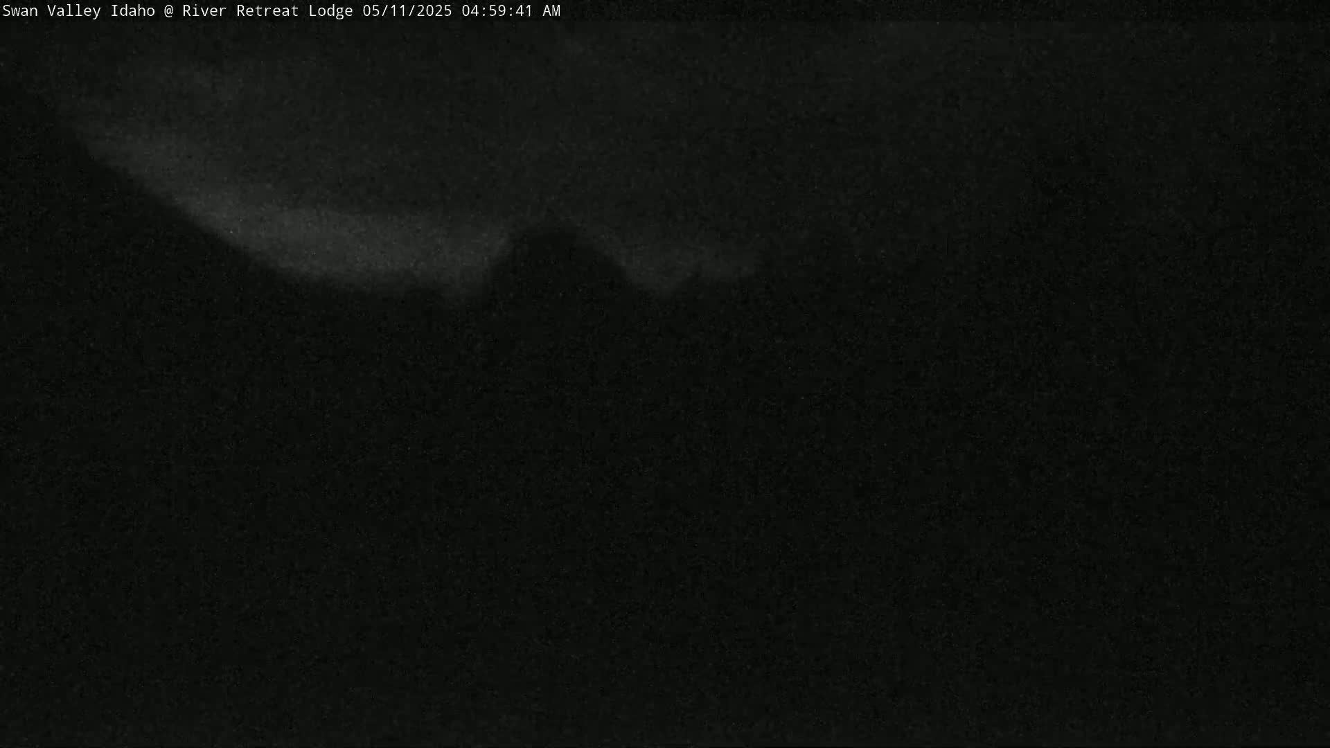 A dark, nighttime image shows a faint, bright band across the top, suggesting a distant, dimly lit landscape under a dark sky.