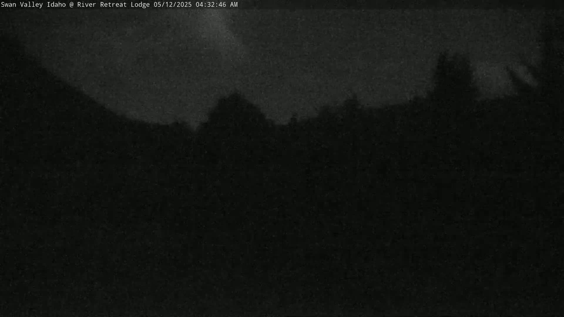A dark, nighttime outdoor scene shows a mostly obscured landscape of trees and hills under a cloudy sky.