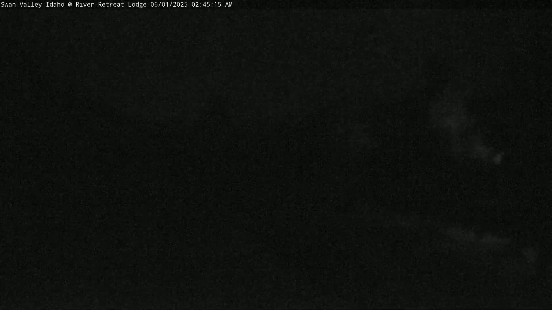 A very dark, almost completely black image, possibly taken at night, shows faint, blurry light features in the distance.