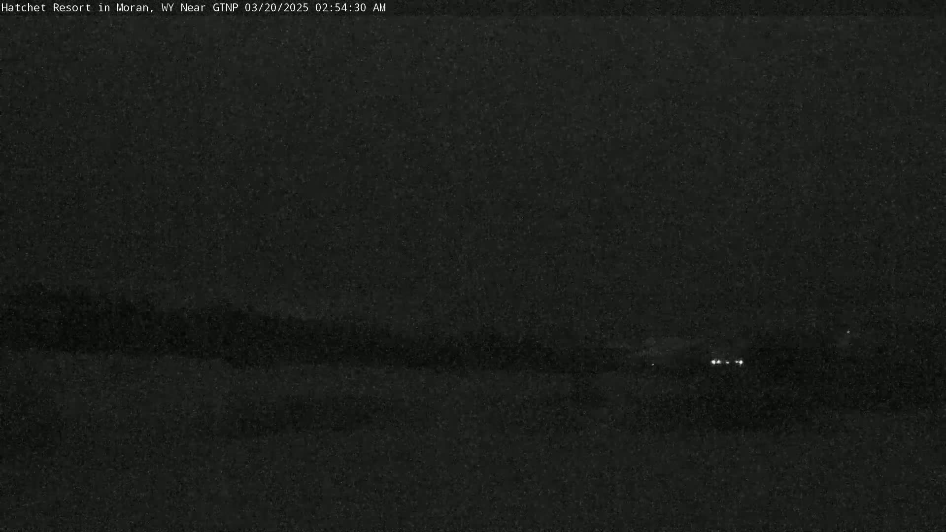 A dark, nighttime landscape is shown with a few small lights visible in the distance.