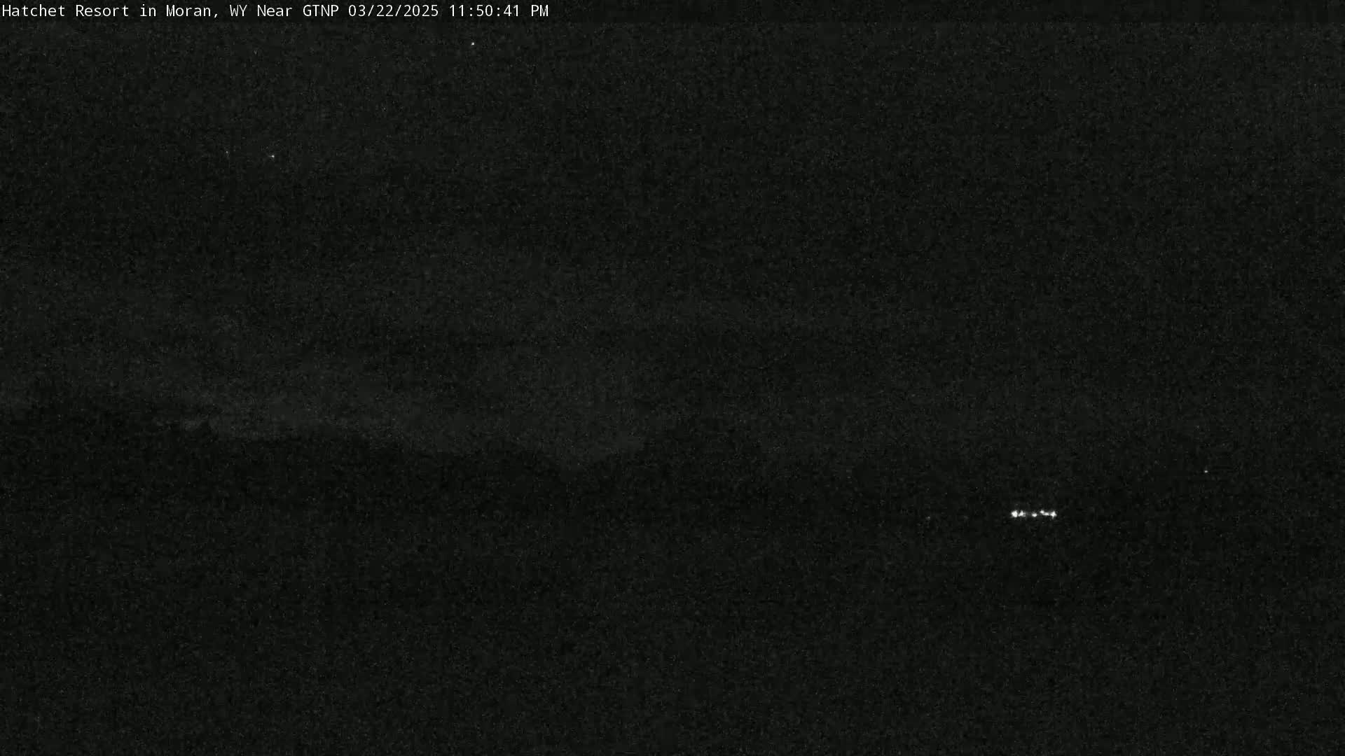 A nighttime, low-light image shows a dark landscape with a few faint lights in the distance.
