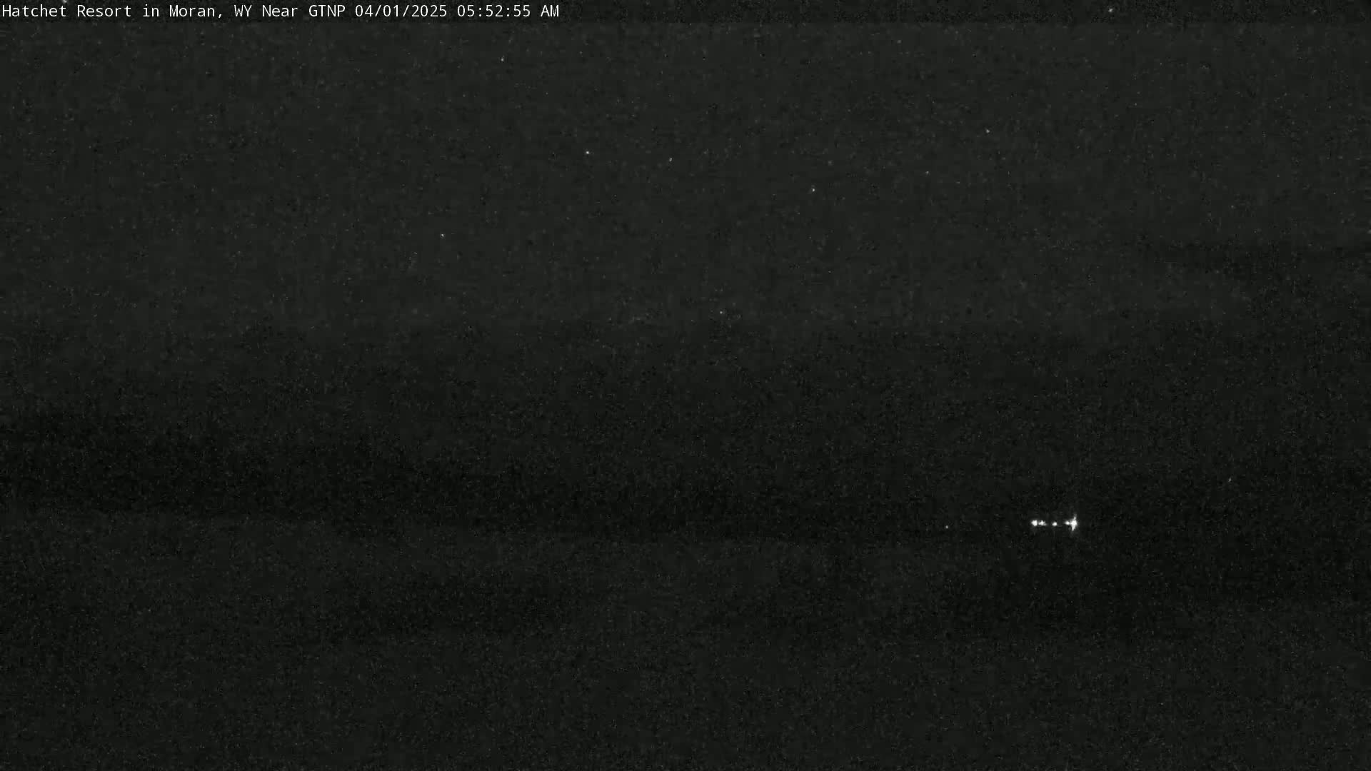 A dark, nighttime scene shows a few faint lights in the distance under a clear sky.