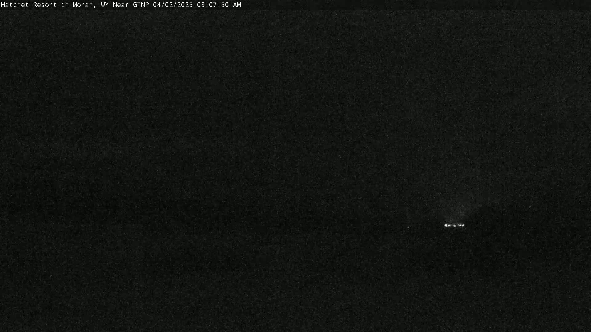 A dark, nighttime scene shows a few small, distant lights on the horizon under a clear, dark sky.