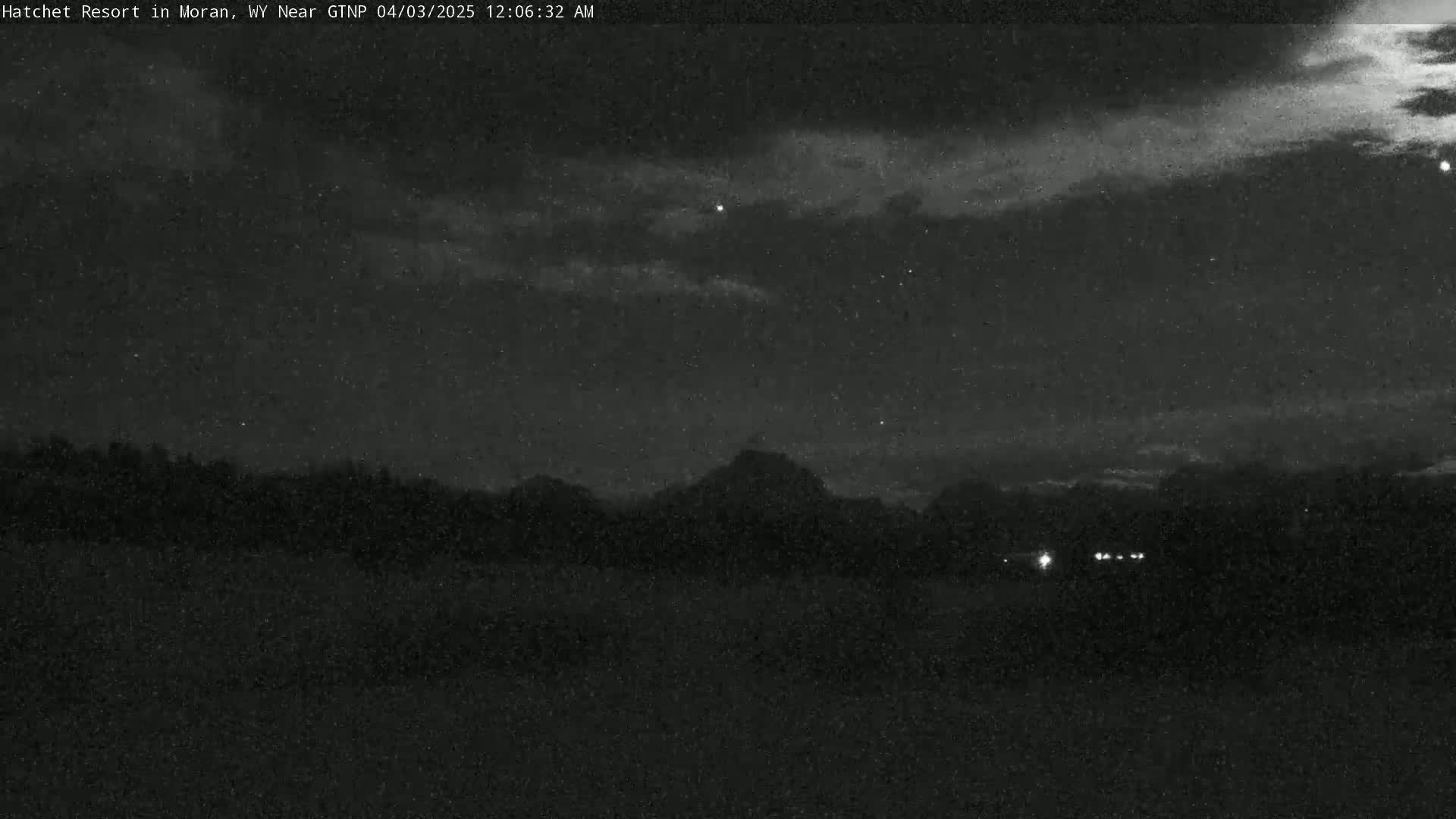 A nighttime, cloudy view shows a dark, silhouetted mountain range in the distance, with a few faint lights visible near the bottom.