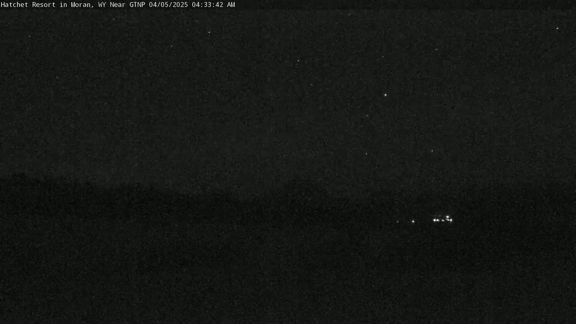 A nighttime, low-light image shows a dark landscape with a few small, distant lights visible.