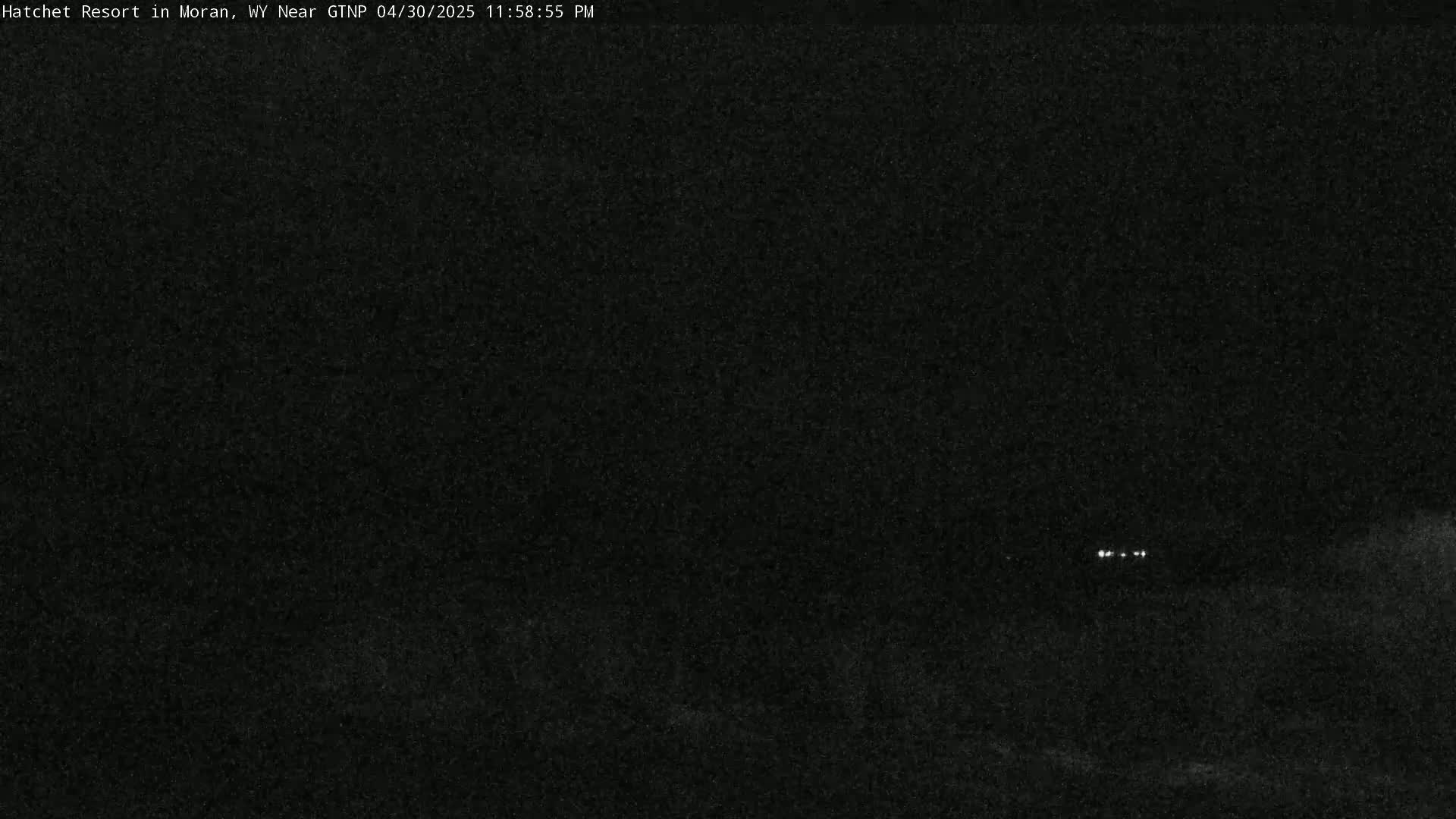 A dark, nighttime scene shows a few faint lights in the distance under a mostly clear sky.
