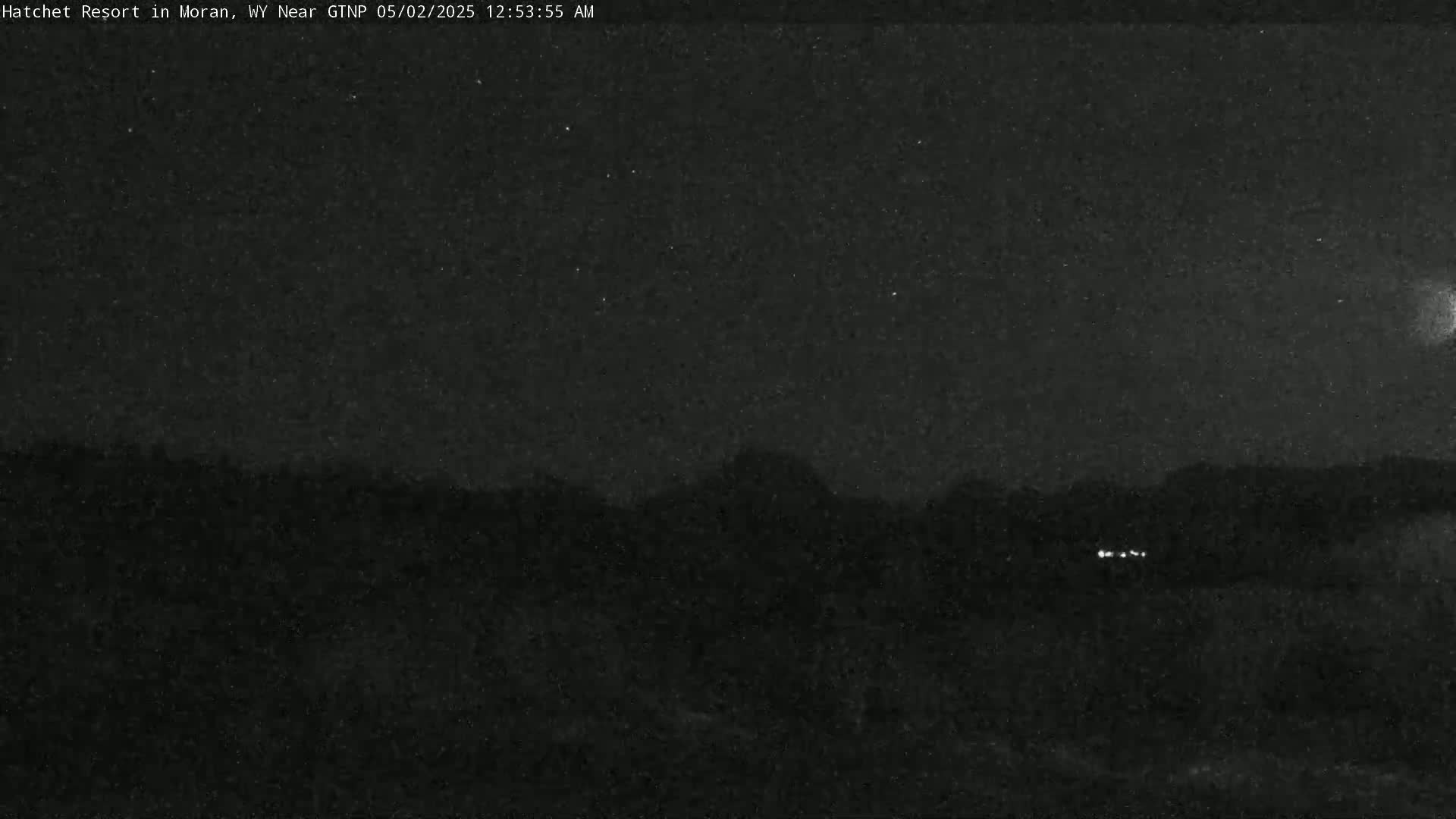 A nighttime view shows dark, silhouetted mountains under a mostly clear, starry sky.