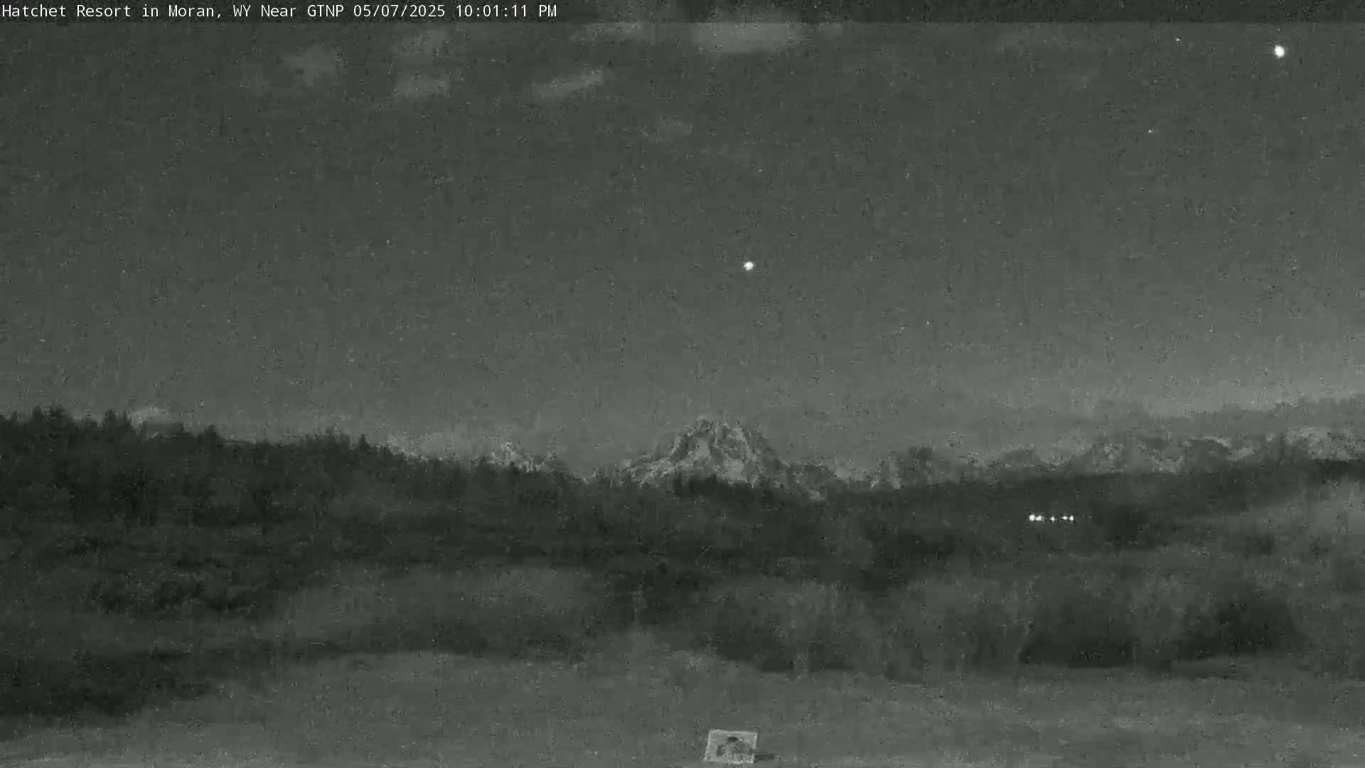 A nighttime, low-light view shows a mountain range silhouetted against a dark sky with a few visible stars.