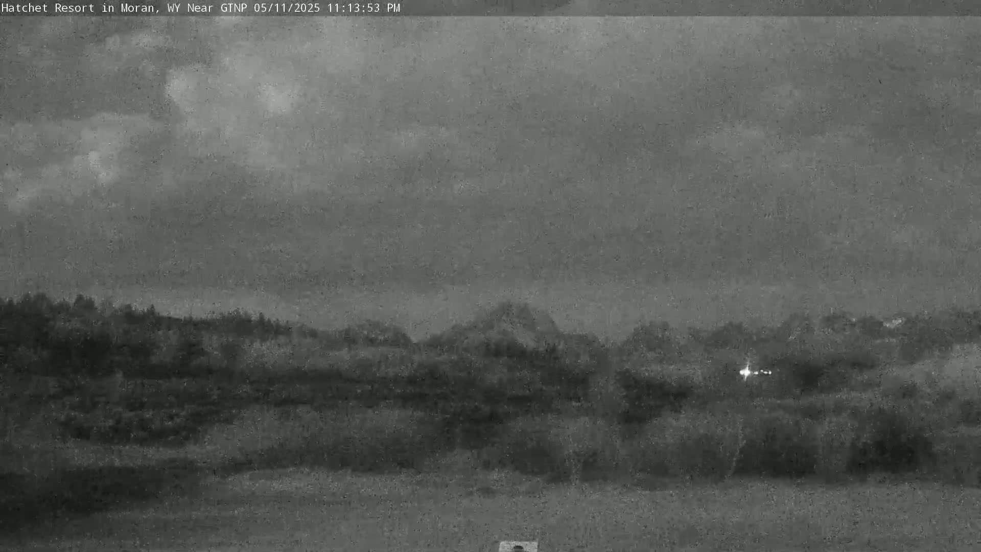 A low-light, overcast view of a landscape shows dark trees and hills under a gray sky.