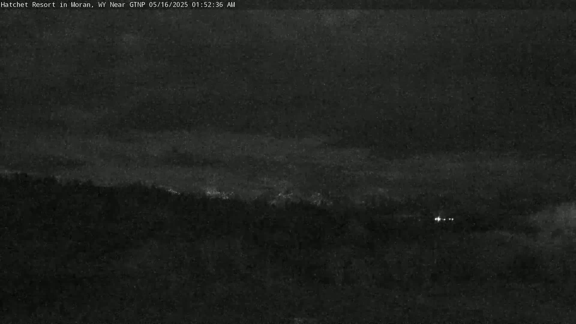 A nighttime view of a dark, tree-covered landscape under a mostly cloudy sky.