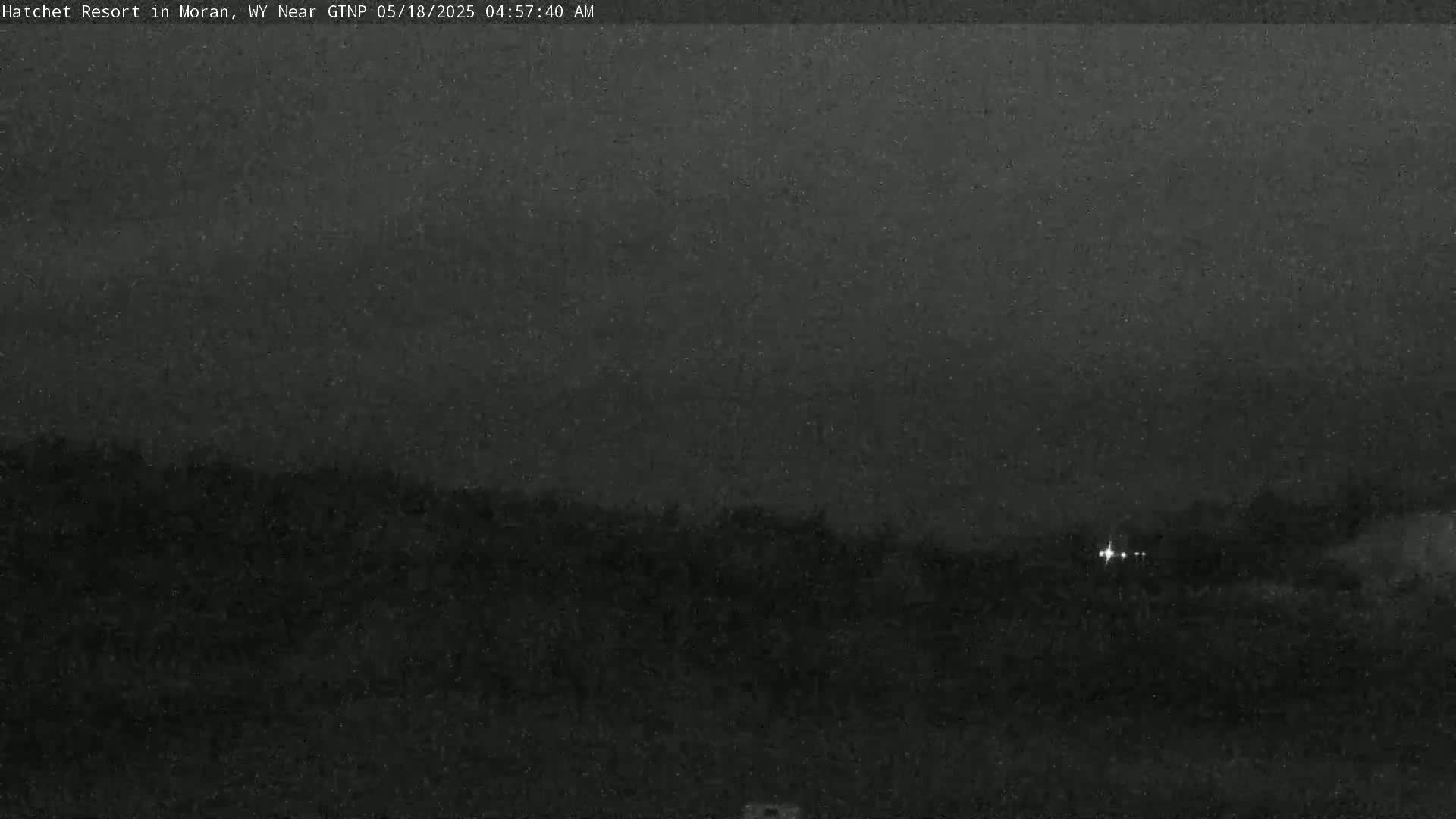 A nighttime, low-light outdoor image shows a dark landscape with a few distant lights.