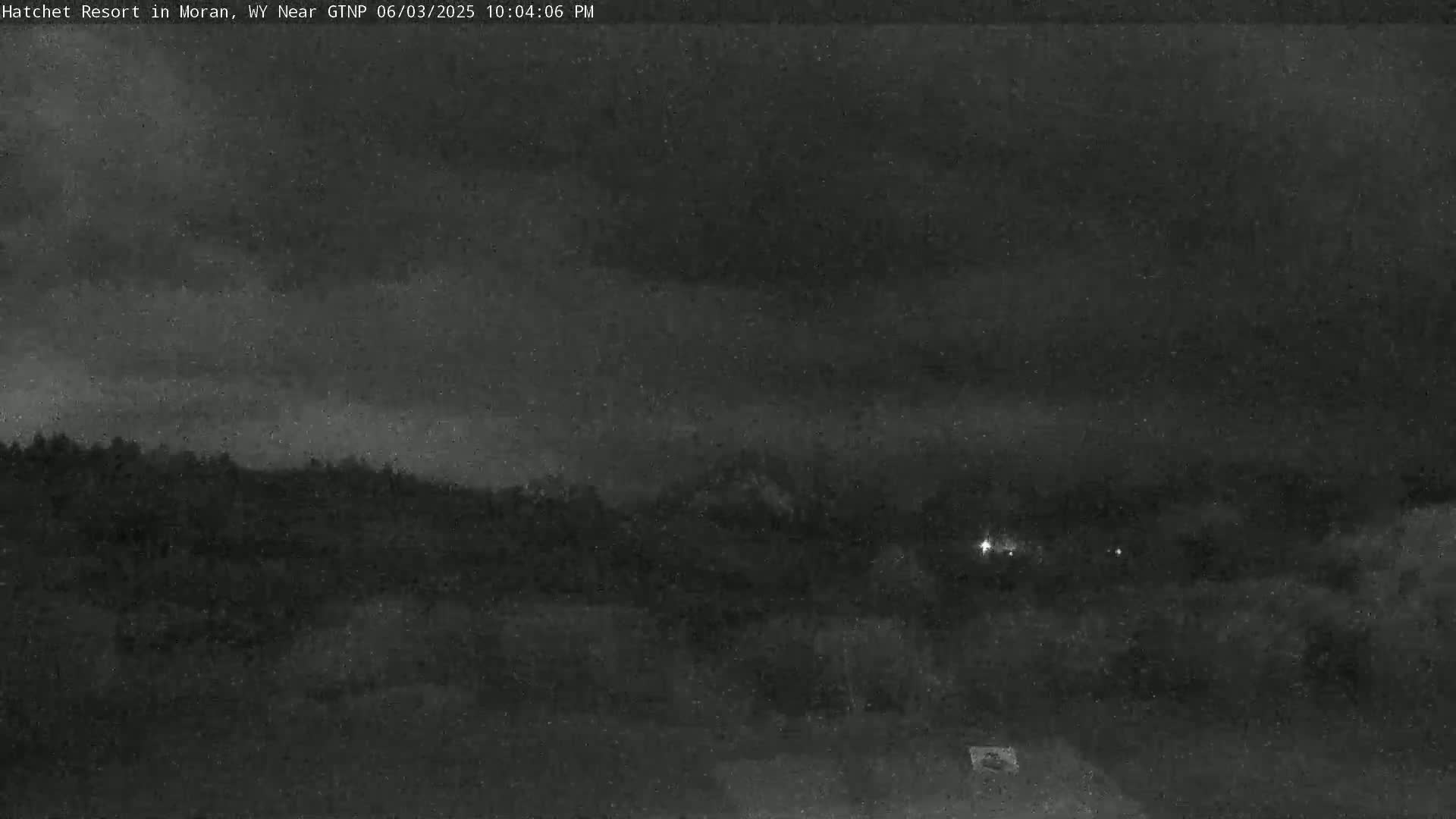A nighttime view shows a dark, overcast sky above a line of dark trees and a flat, dark foreground.