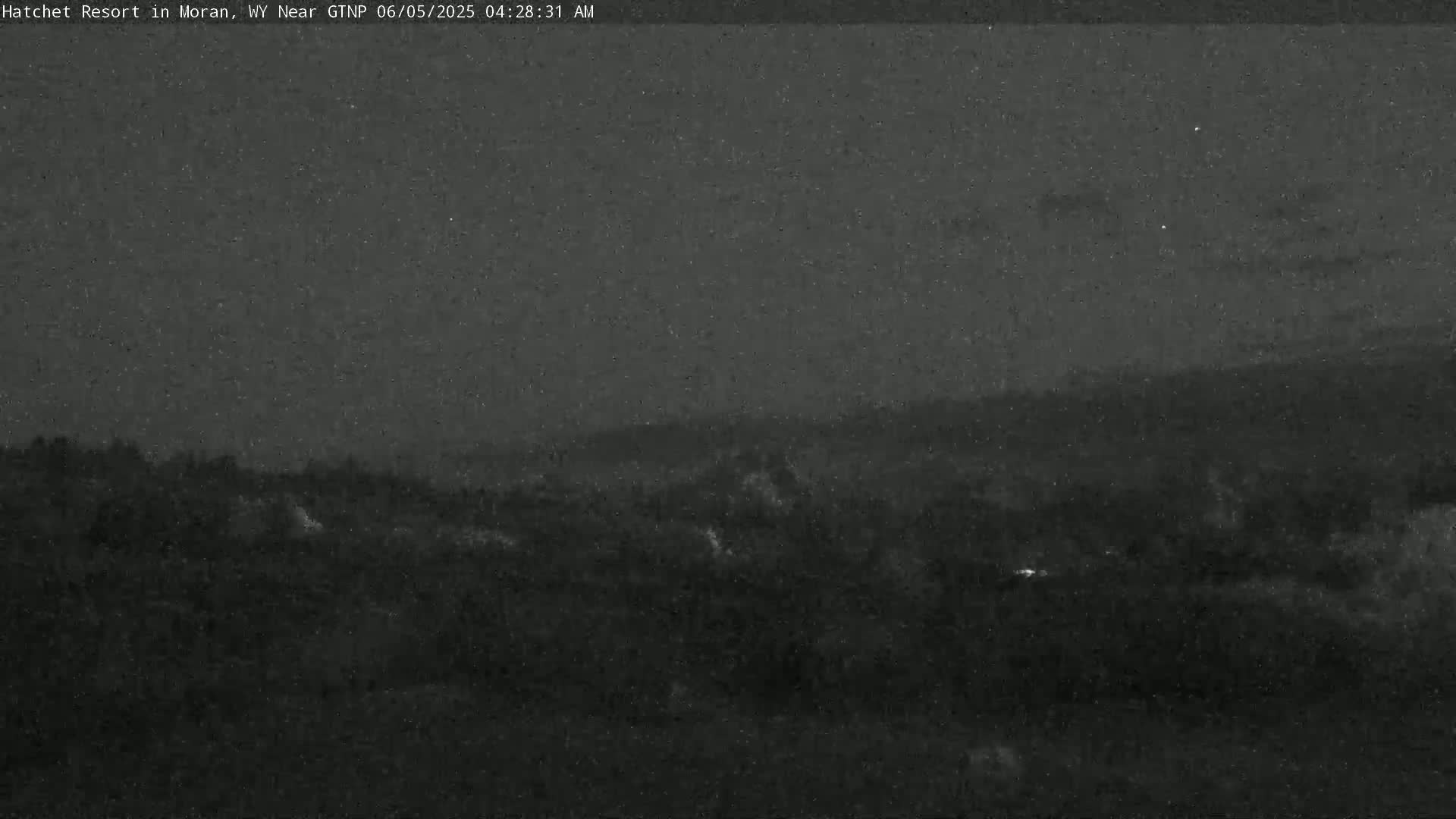 A dark, nighttime view of a hilly landscape under a mostly clear sky.