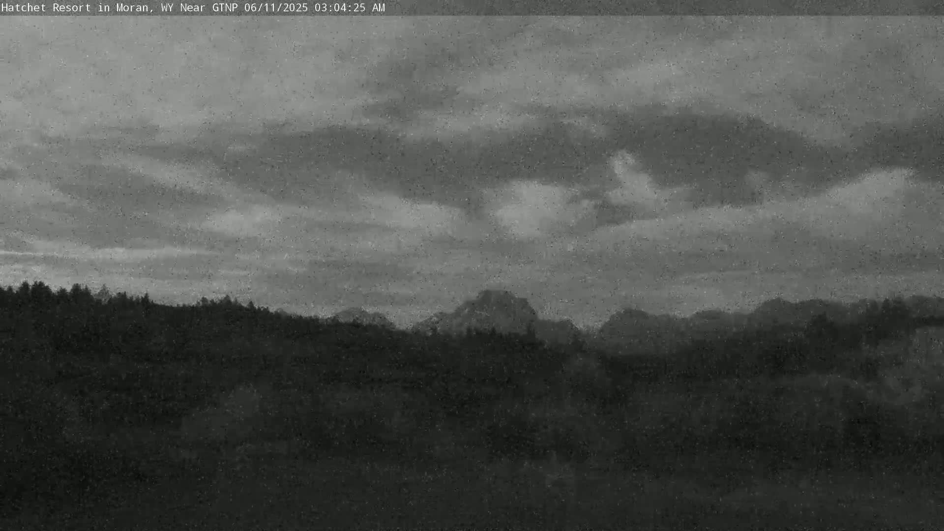 A dark, cloudy sky hangs over a line of dark, forested hills and mountains.