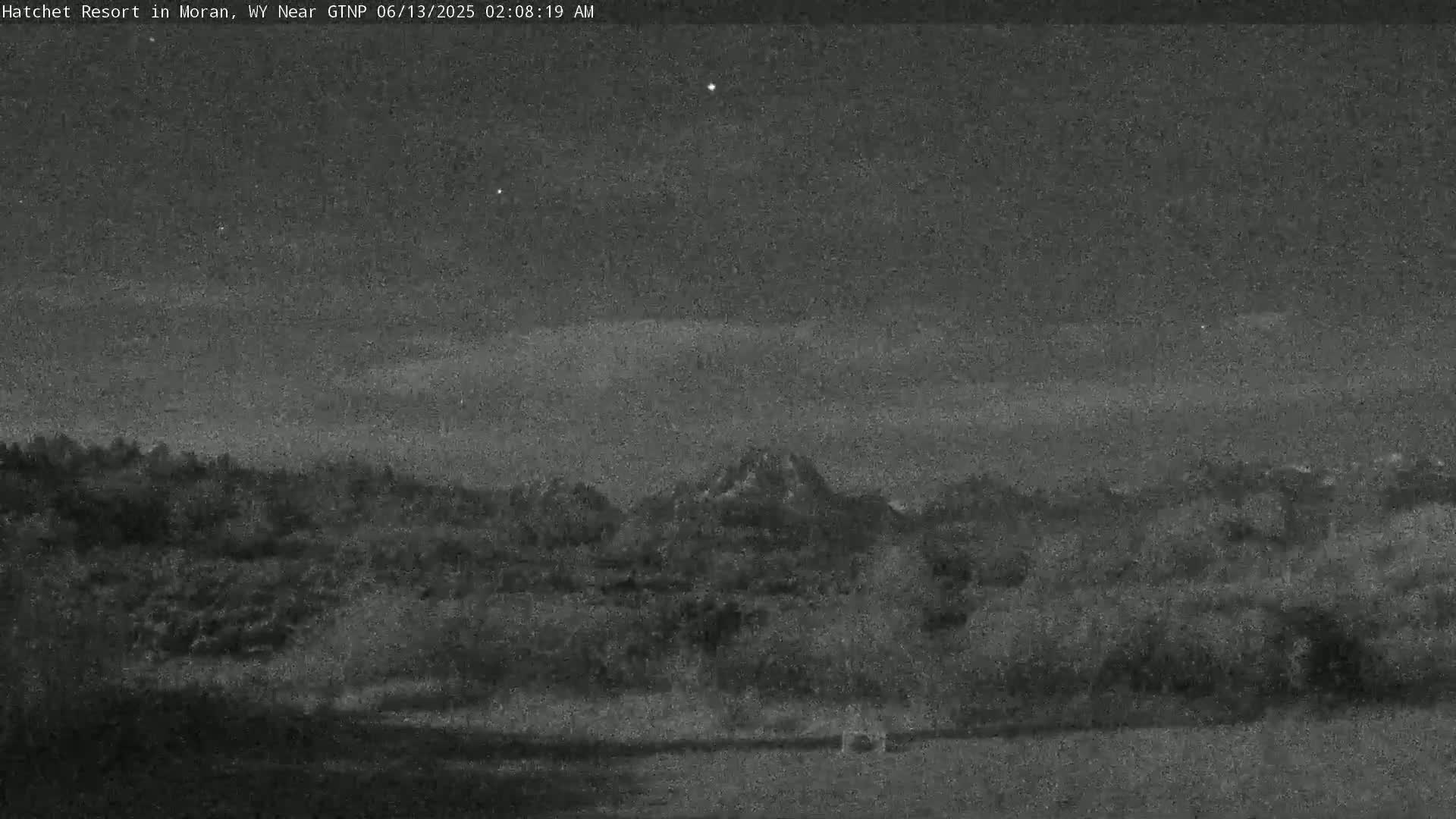 A nighttime, low-light view shows a dark landscape with hills and a few stars visible in the sky.